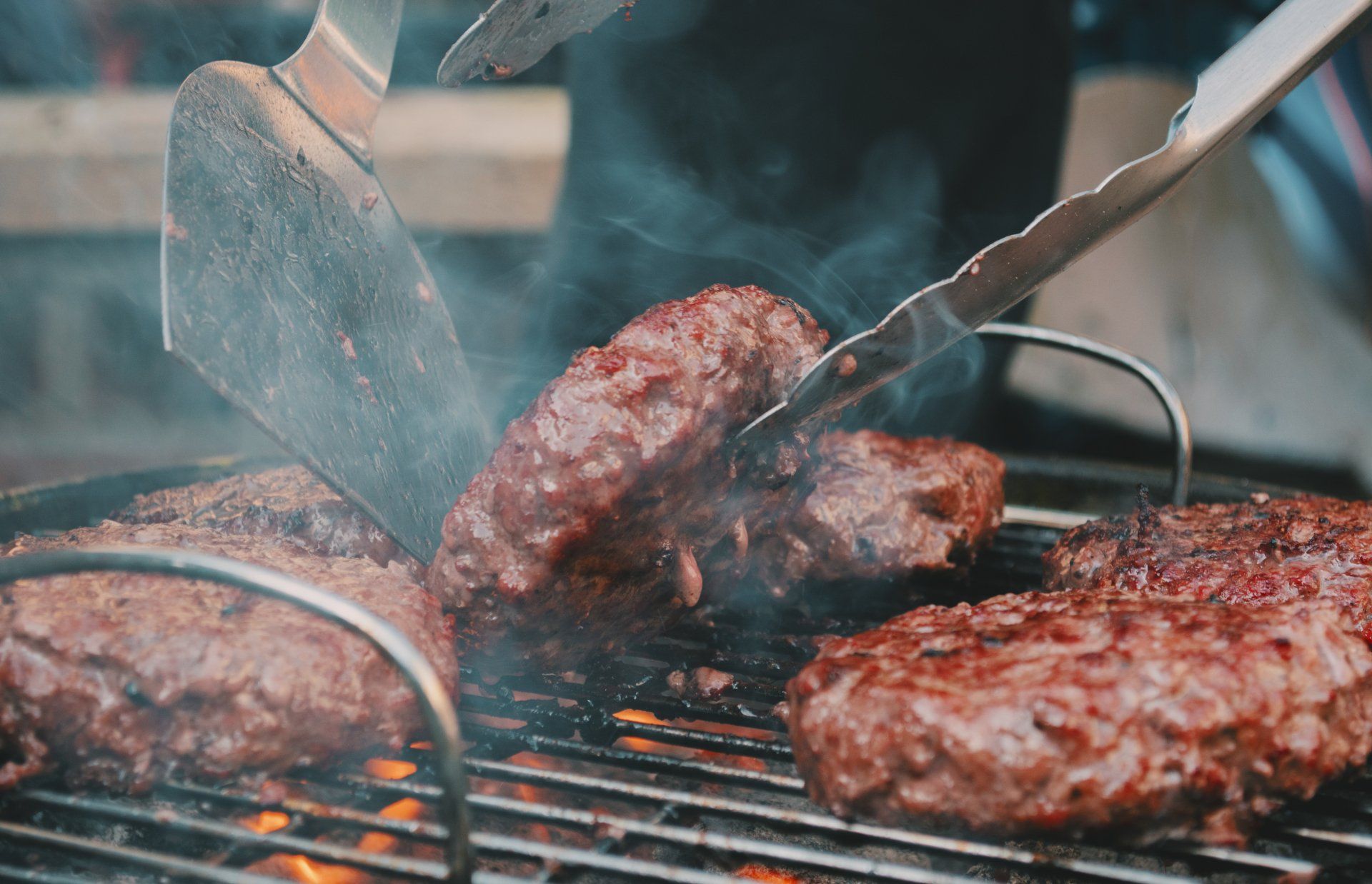A person is cooking hamburgers on a grill with a spatula.
