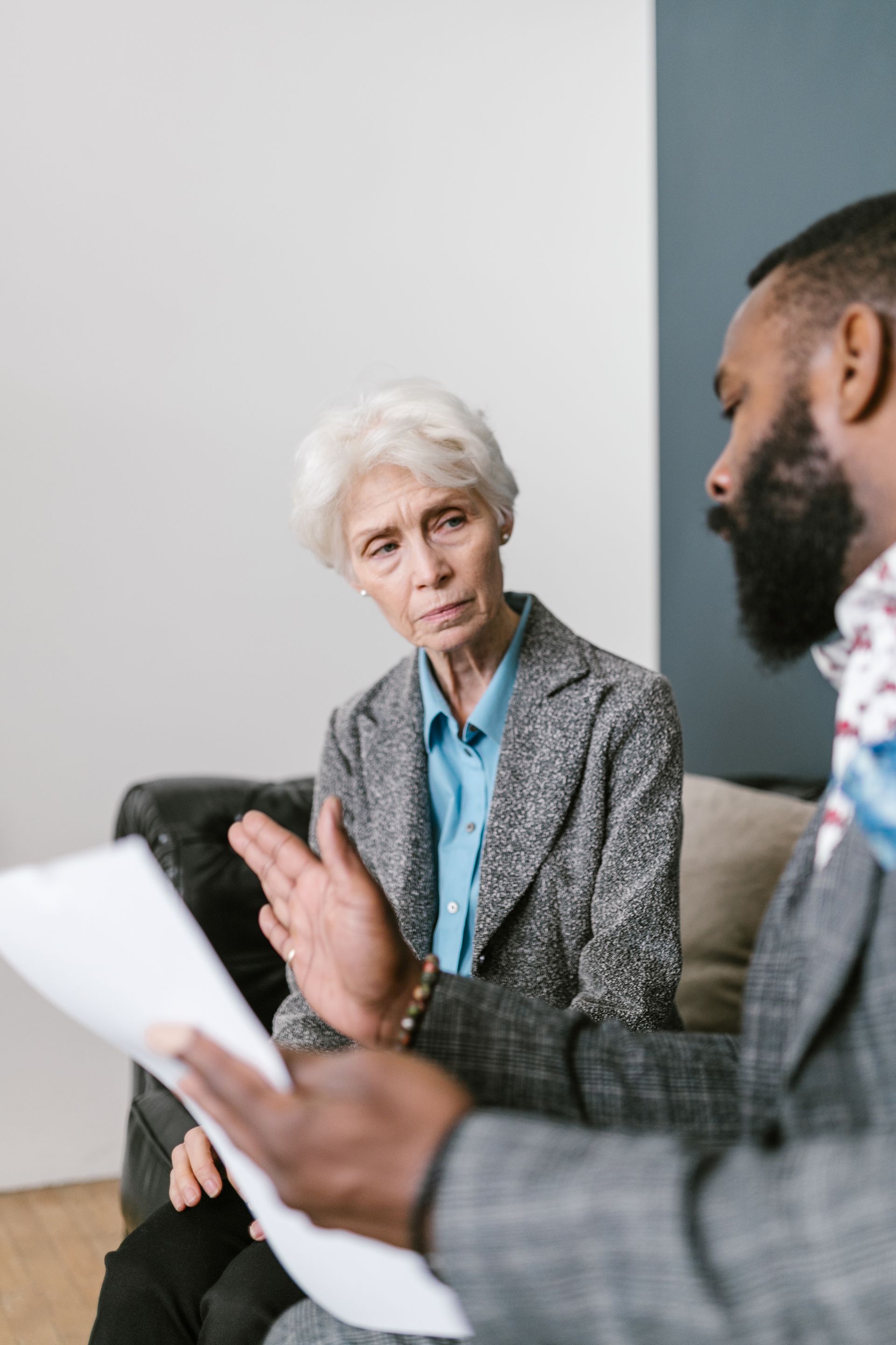 A man is talking to an older woman while holding a piece of paper.
