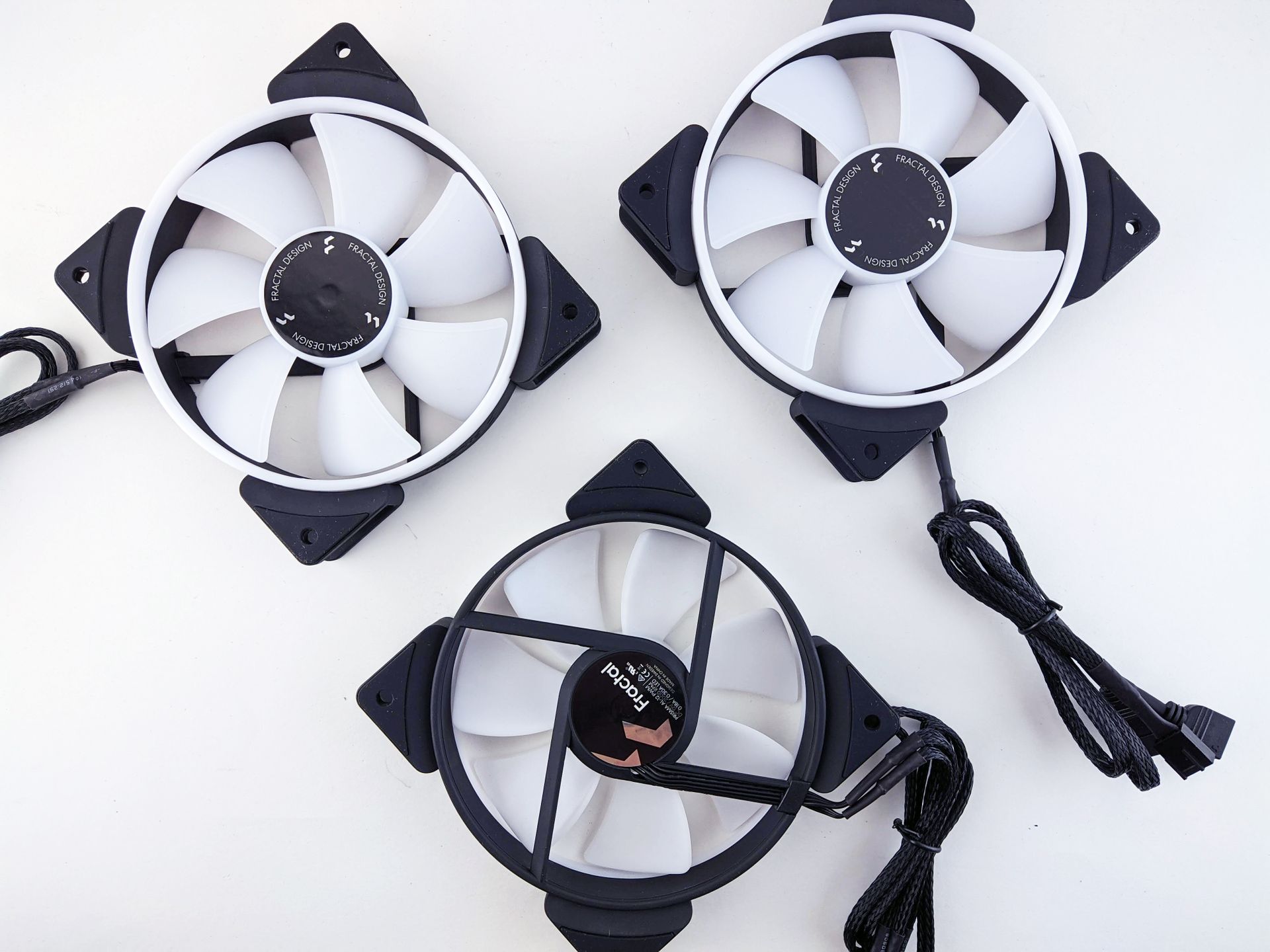 Three white PC cooling fans on a white background, two with black corner mounts and attached cables