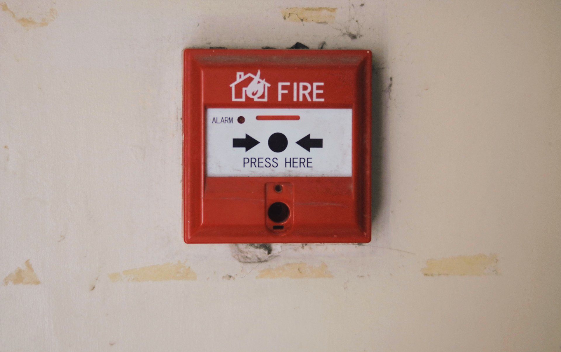 A red fire alarm is hanging on a white wall.