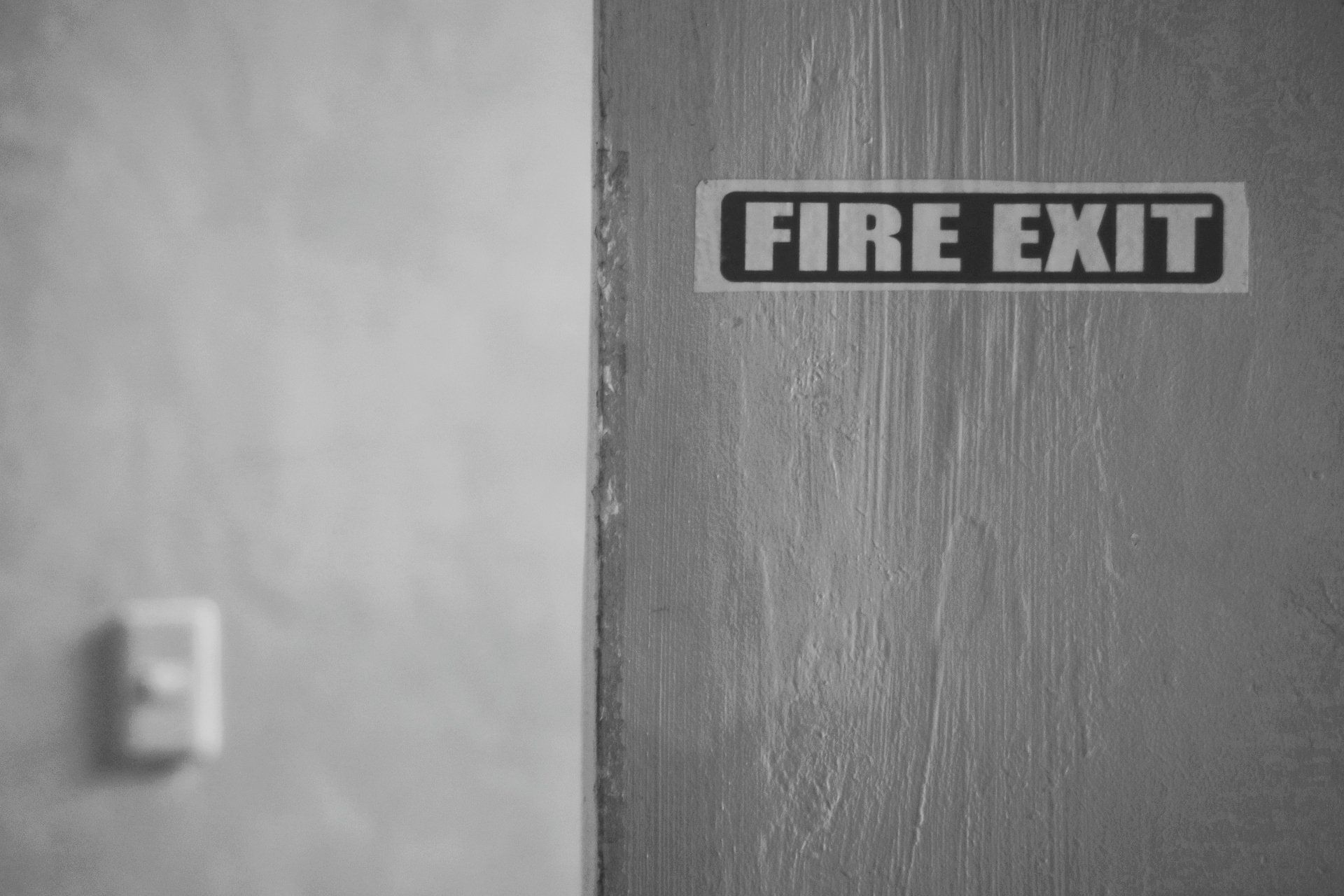 A black and white photo of a fire exit sign on a door.