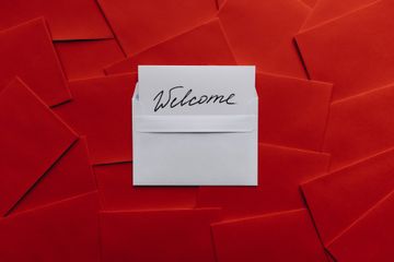 White note reading “Welcome” on a red background of overlapping paper squares.