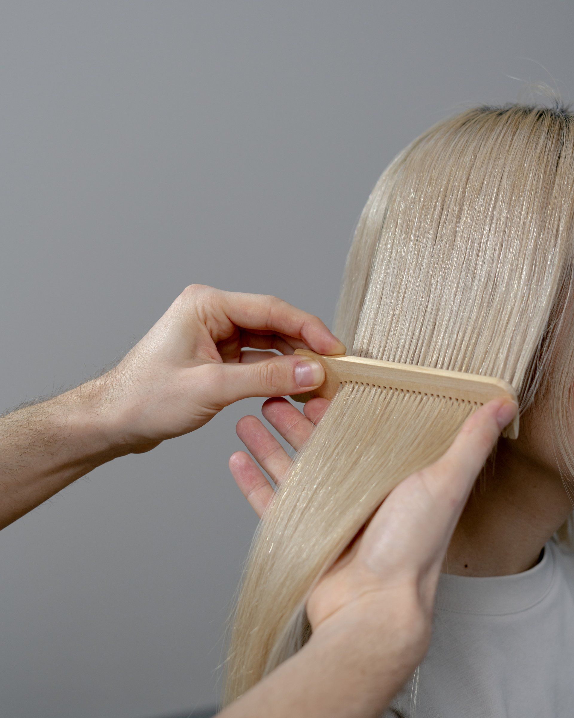 A person is brushing a woman 's blonde hair with a wooden comb.