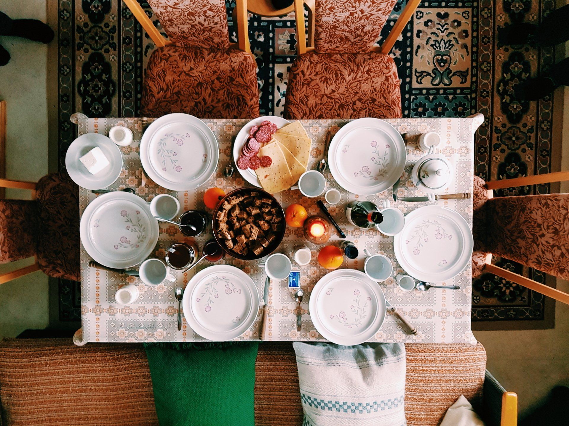 Overhead shot of a dining table set for a meal. Plates, food, and drinks arranged on a floral tablecloth.