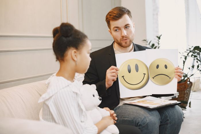 Therapist showing smiley and sad face cards to a seated client in a counseling office