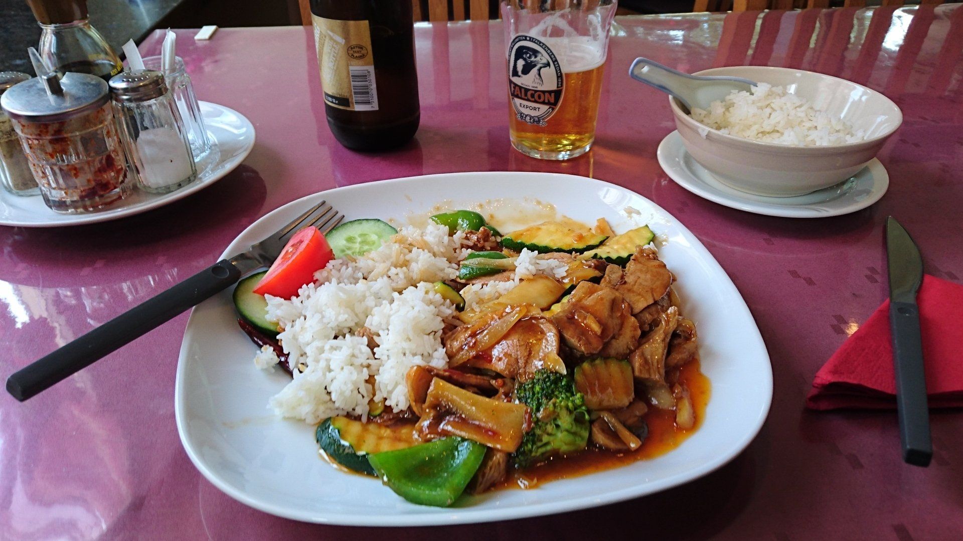 A plate of food with rice and vegetables on a table next to a bottle of beer.