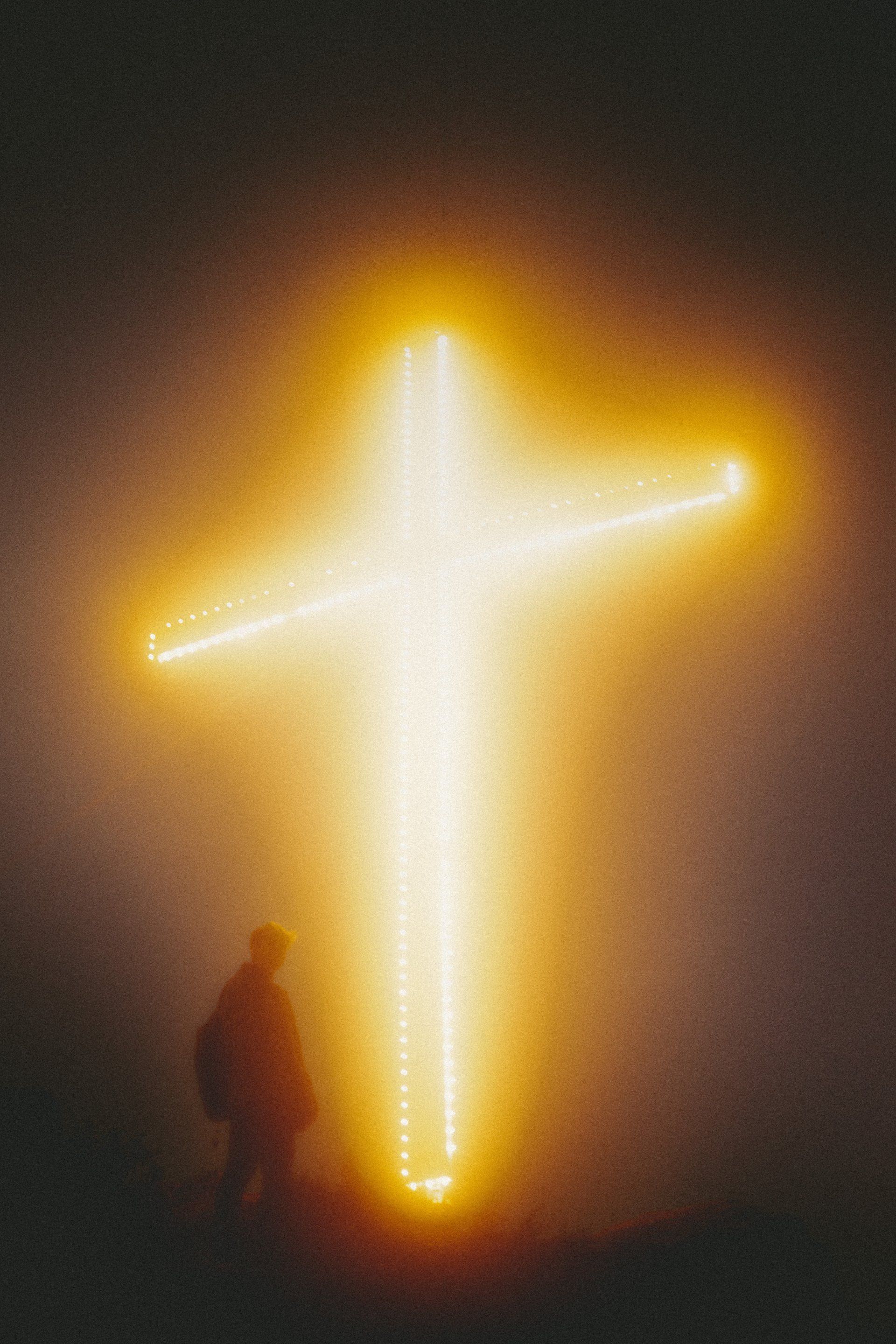 A man is standing in front of a brightly lit cross.