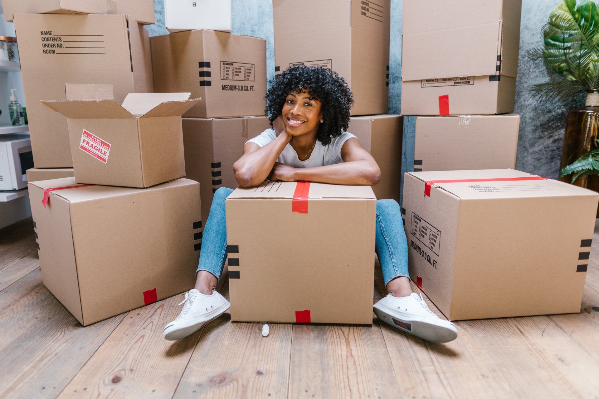 A woman is sitting on a cardboard box in front of a pile of cardboard boxes.