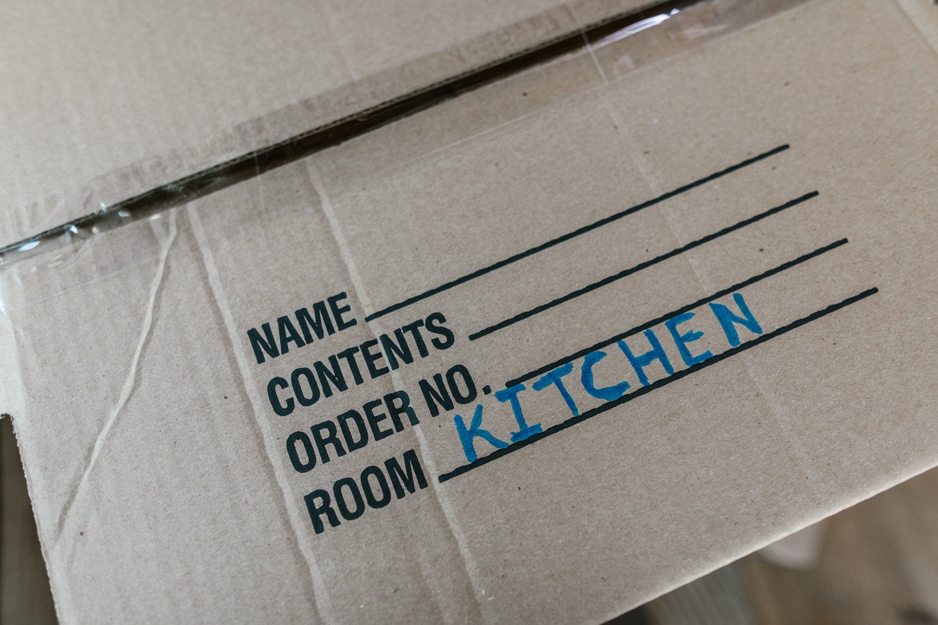 A cardboard box with the words `` name contents order no kitchen room '' written on it.