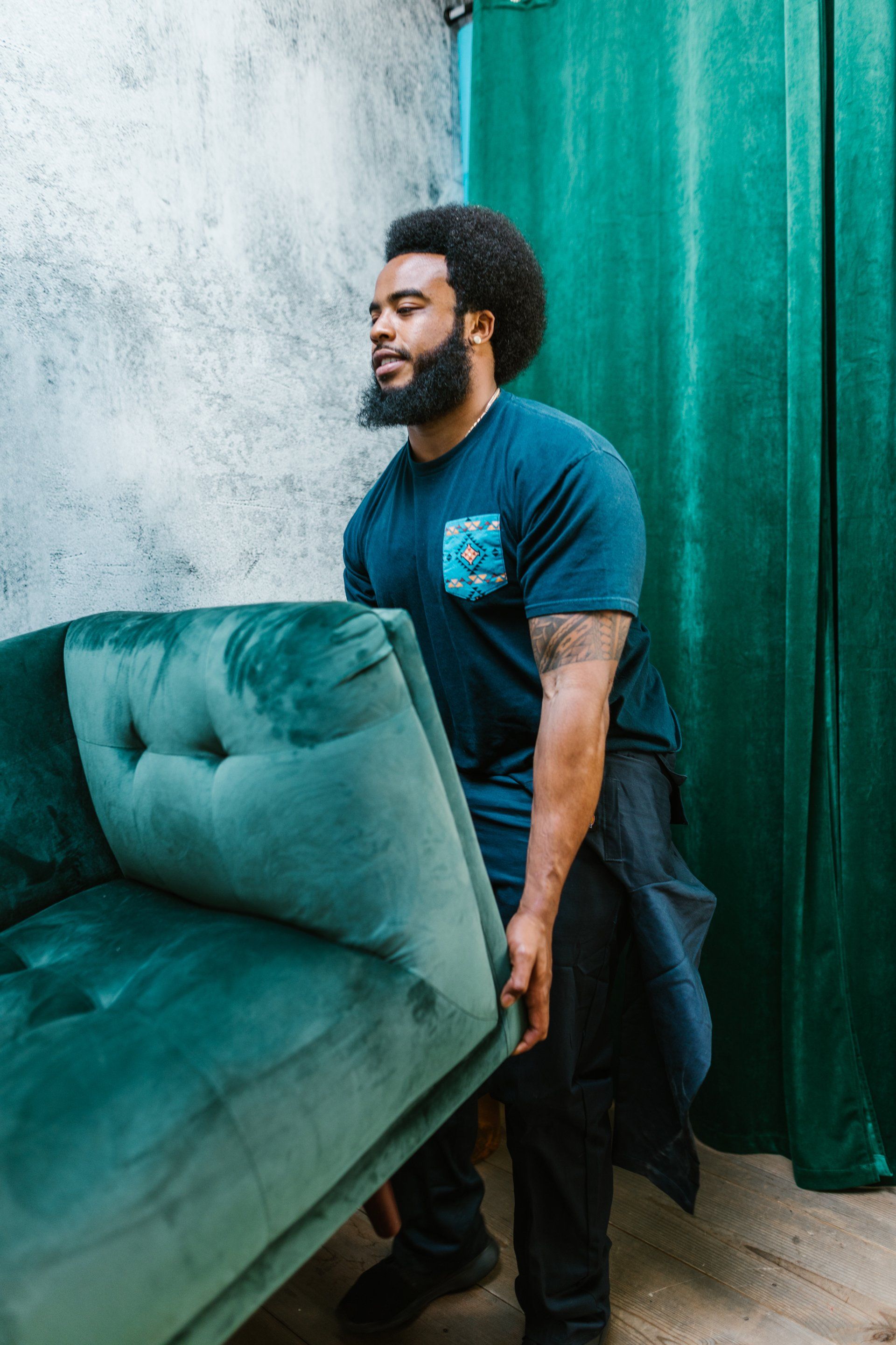 A man is holding a green couch in a room.
