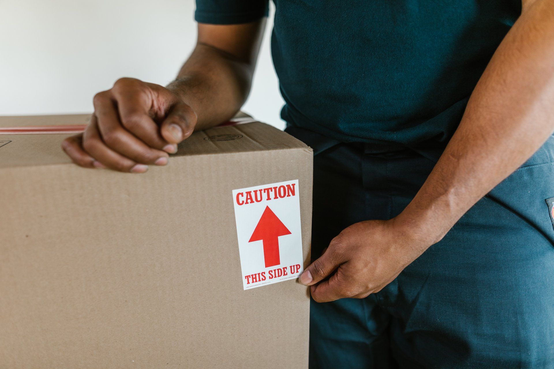 Person placing a red “Caution This Side Up” label on a cardboard box