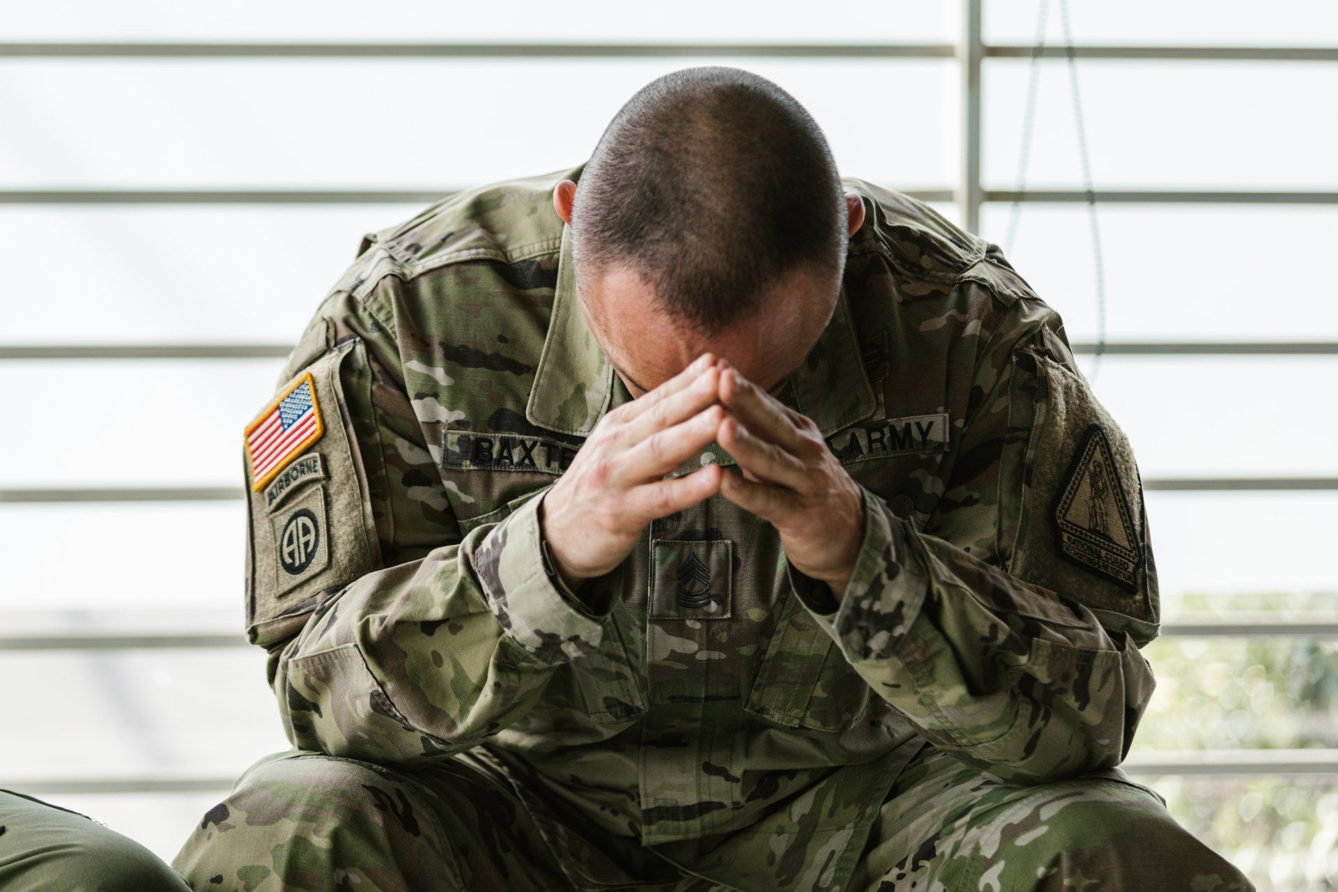 A soldier is sitting down with his head in his hands.