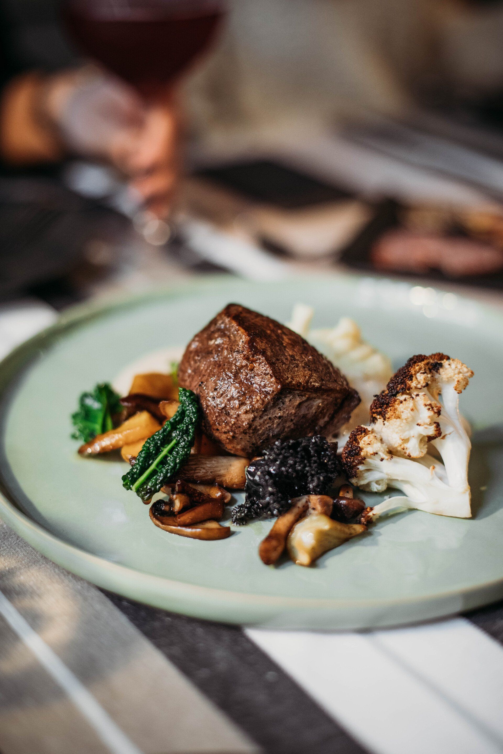 Plate of seared steak, mashed potatoes, roasted vegetables, and cauliflower. The plate is light green.