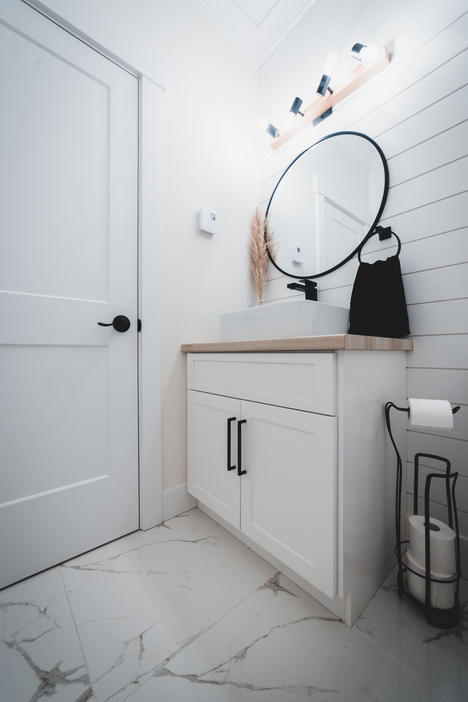 Modern white bathroom with vanity, round mirror, and shiplap wall.