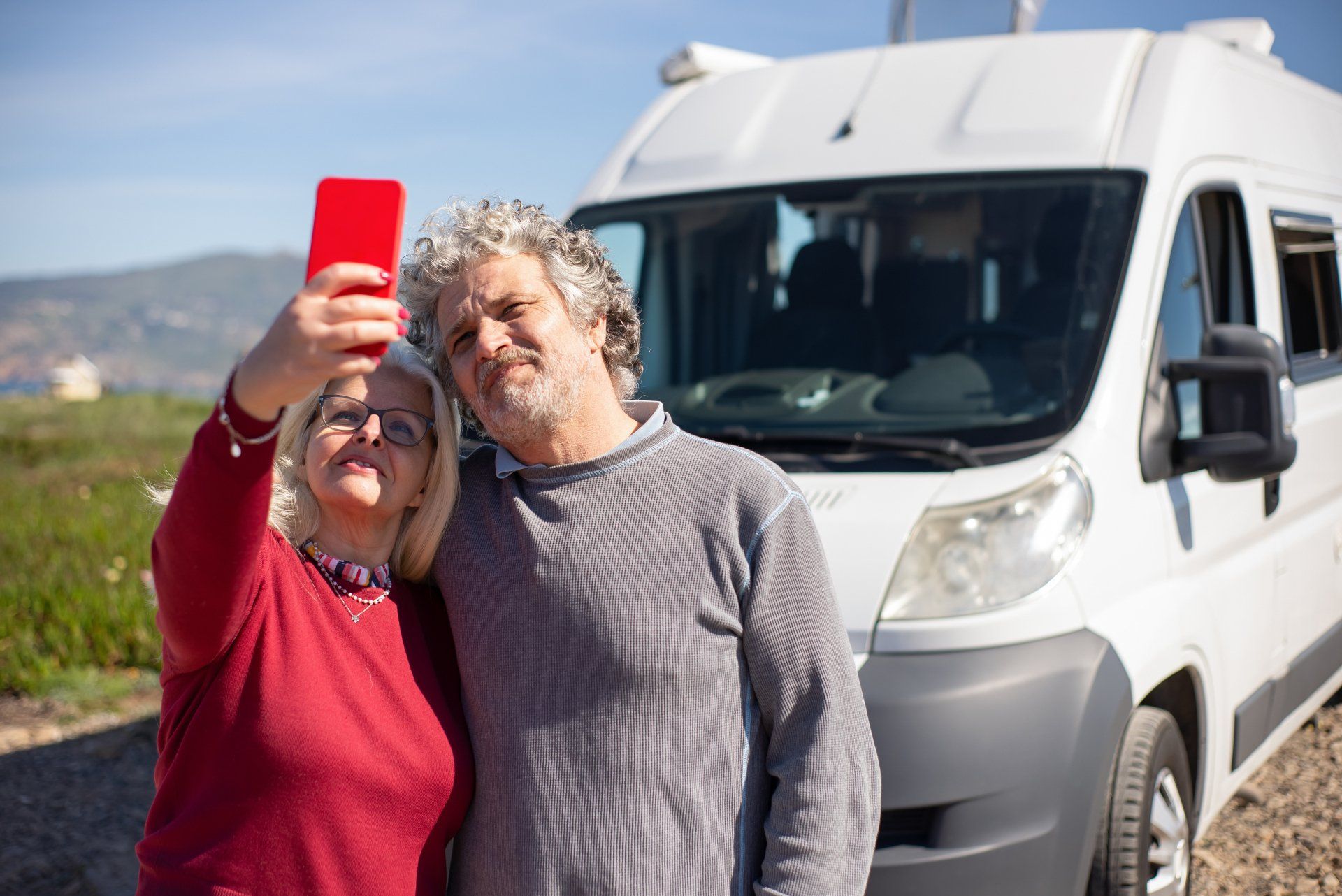 A man and a woman are taking a selfie in front of a camper van.
