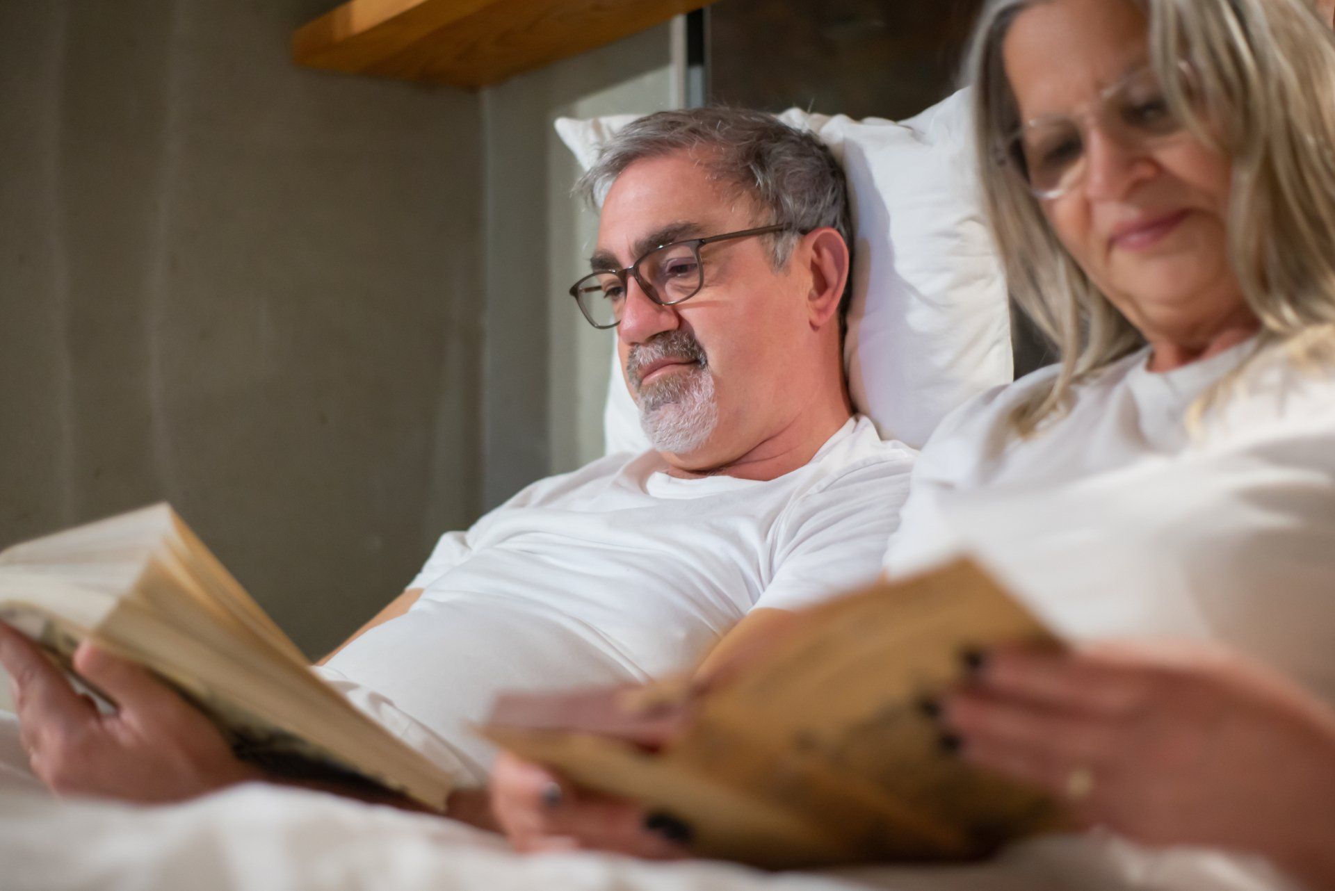 A man and a woman are laying in bed reading books.