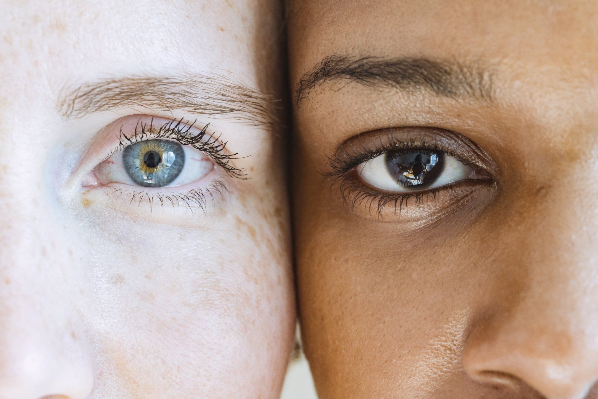 A close up of two women 's eyes , one white and one black , standing next to each other.