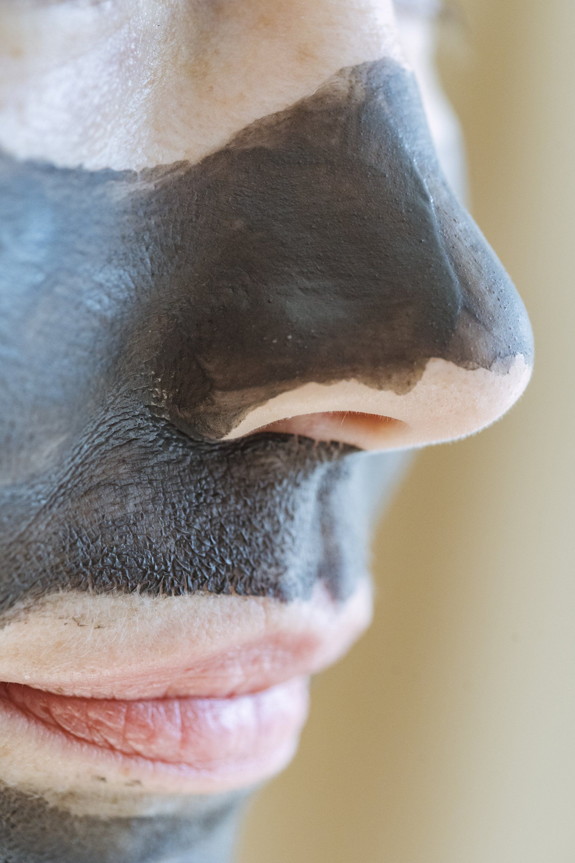 Person with dark gray facial mask applied to face, nose, and mouth, with light skin visible on the upper forehead