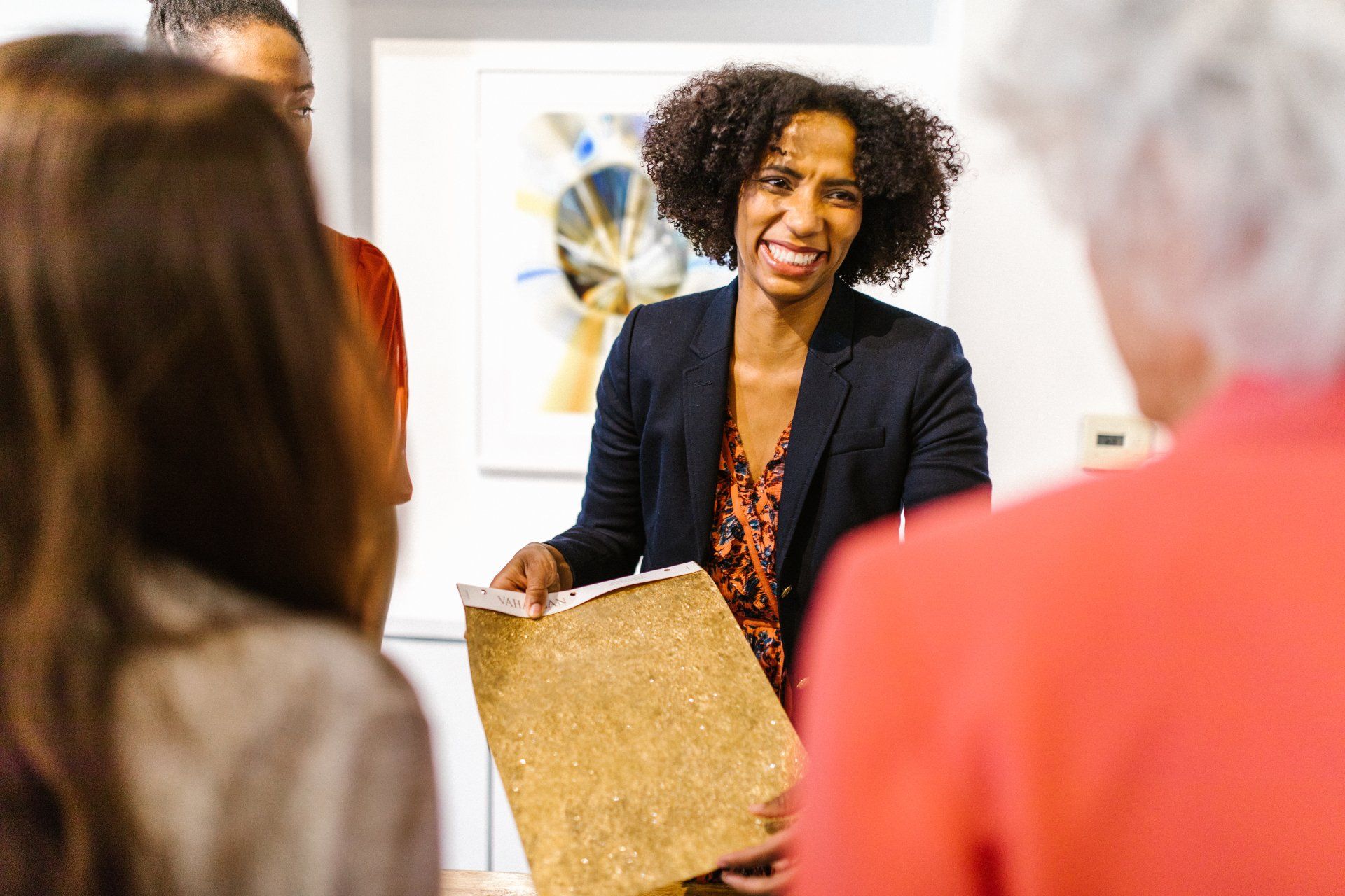 Woman with curly hair presenting a beige material to a group in an art gallery.