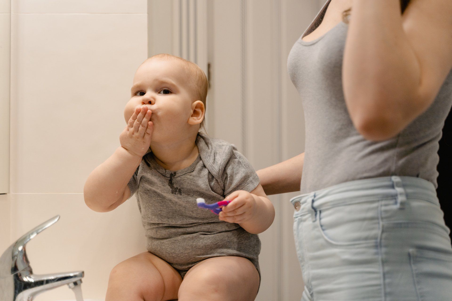 A baby is brushing his teeth in front of a mirror while sitting on a toilet.