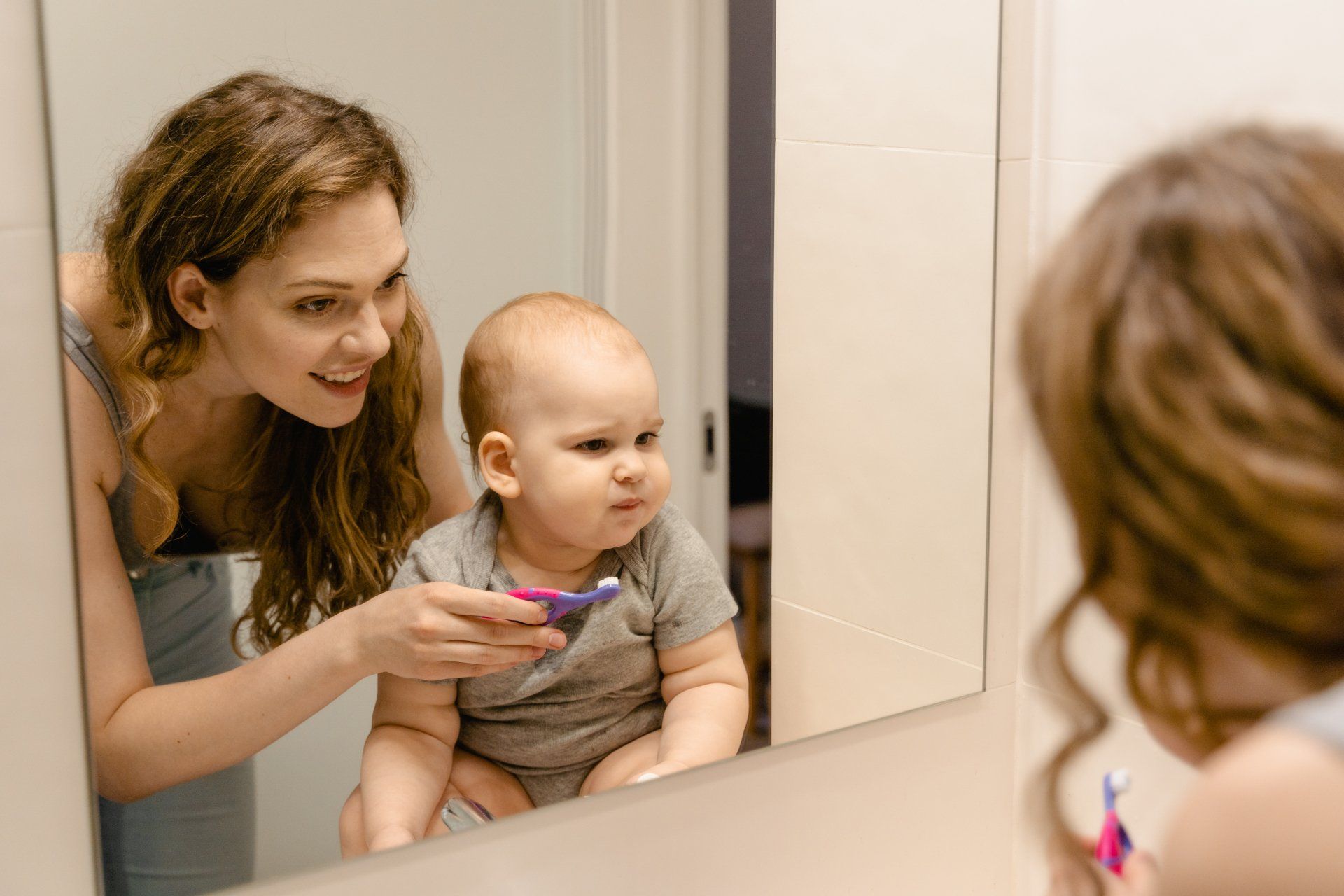 A woman is brushing her baby 's teeth in front of a mirror.