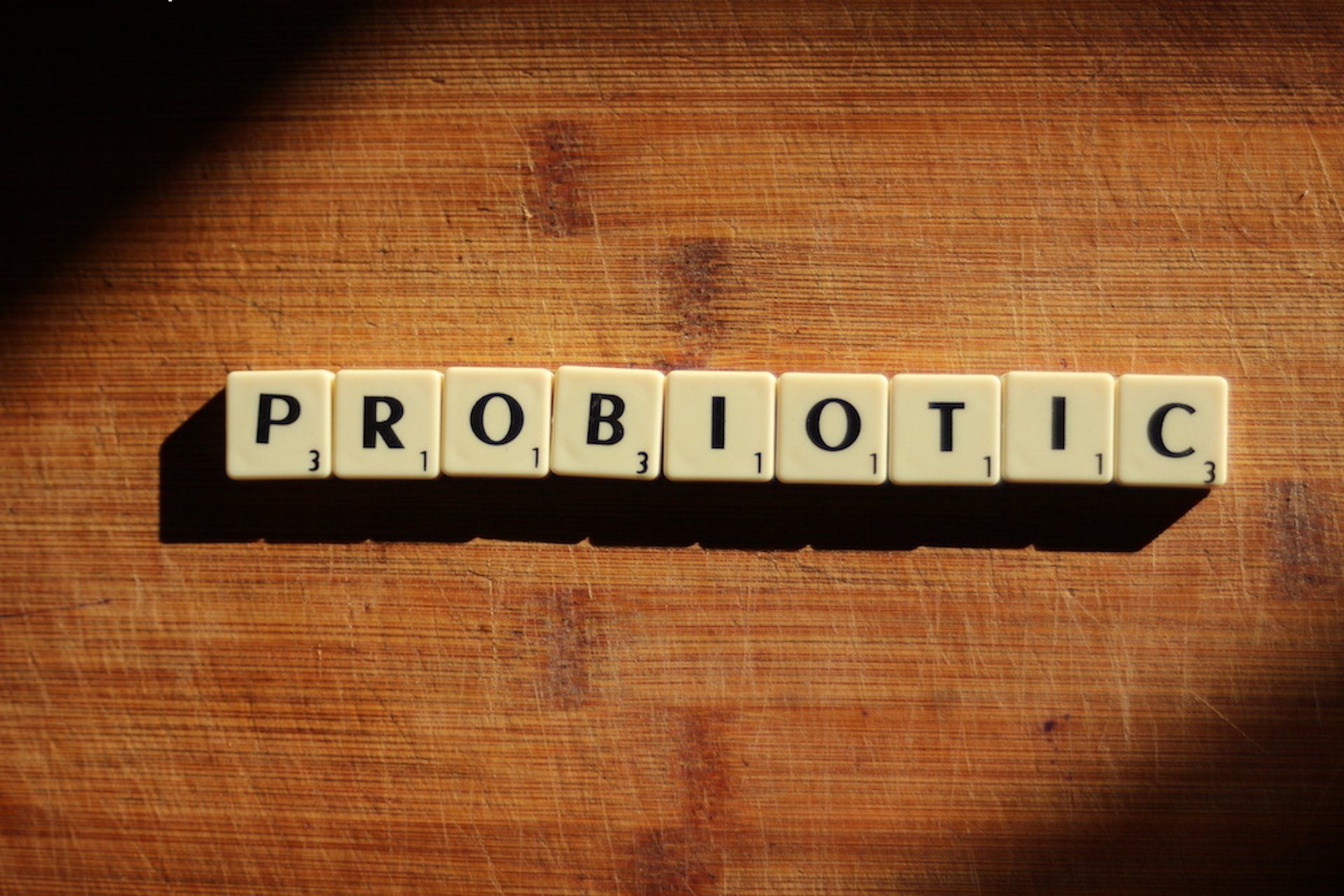 Scrabble tiles spelling “PROBIOTIC” on a black tray over a wooden surface