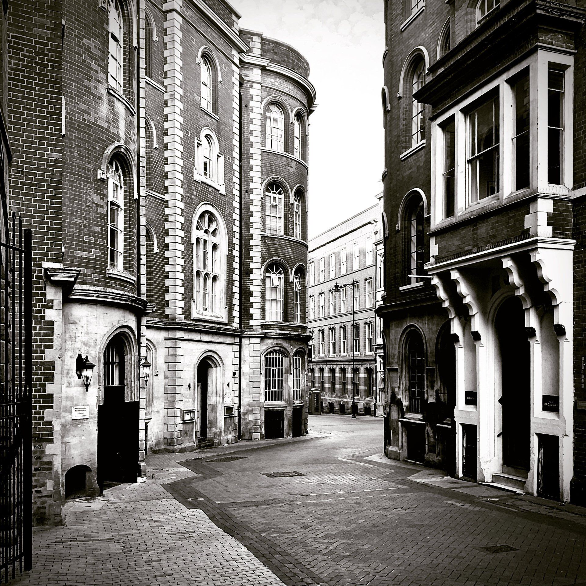 A black and white photo of a narrow street between two brick buildings