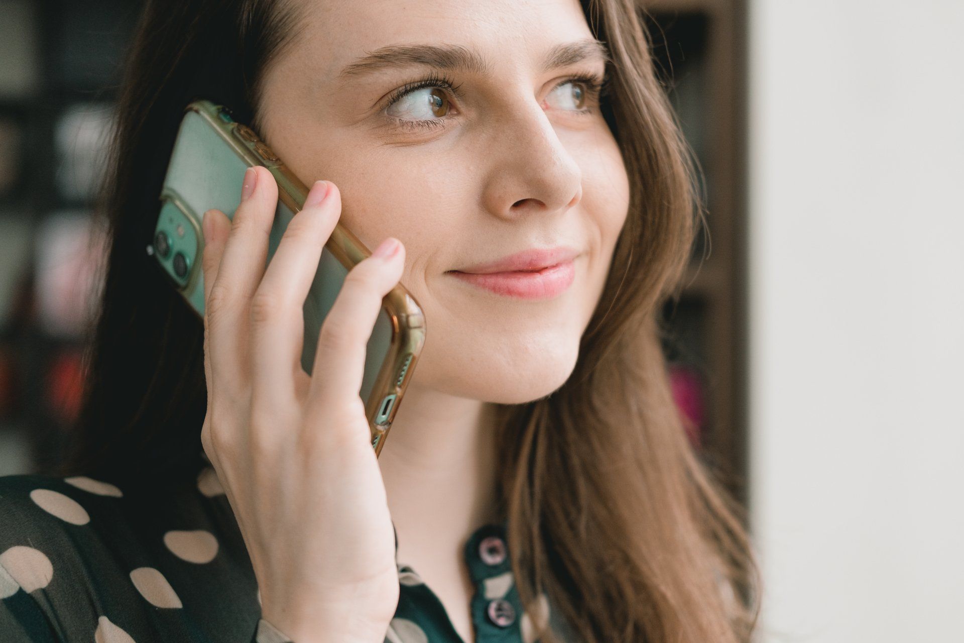 A woman is smiling while talking on a cell phone.