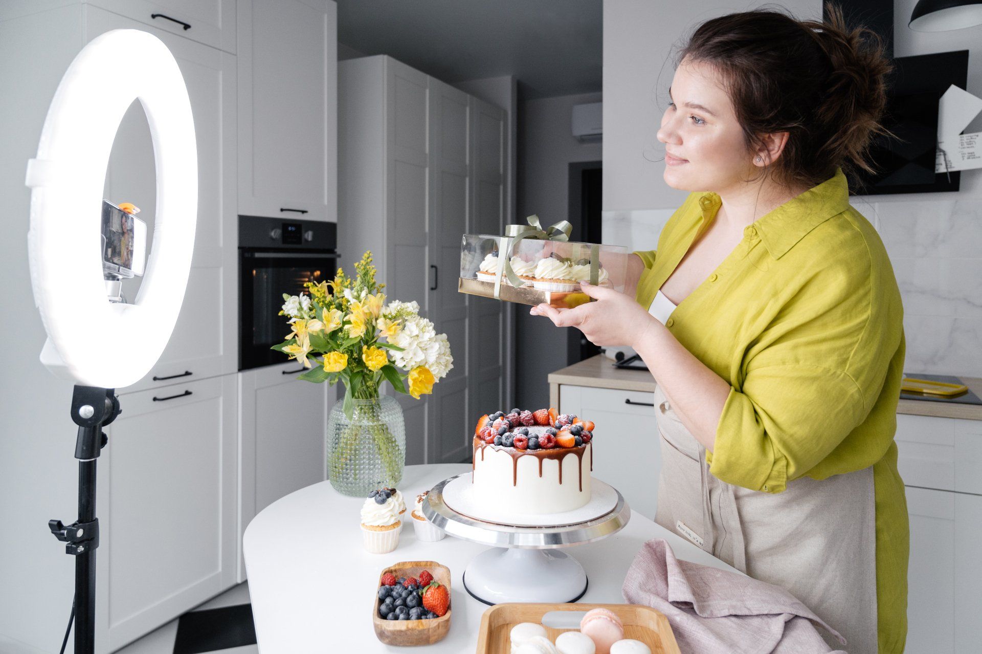 A woman is holding a cake in front of a ring light.