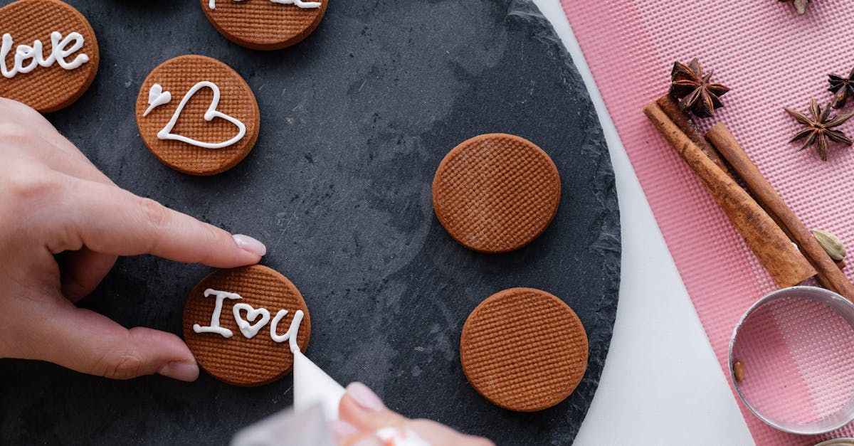 A person decorates round cookies with white icing;