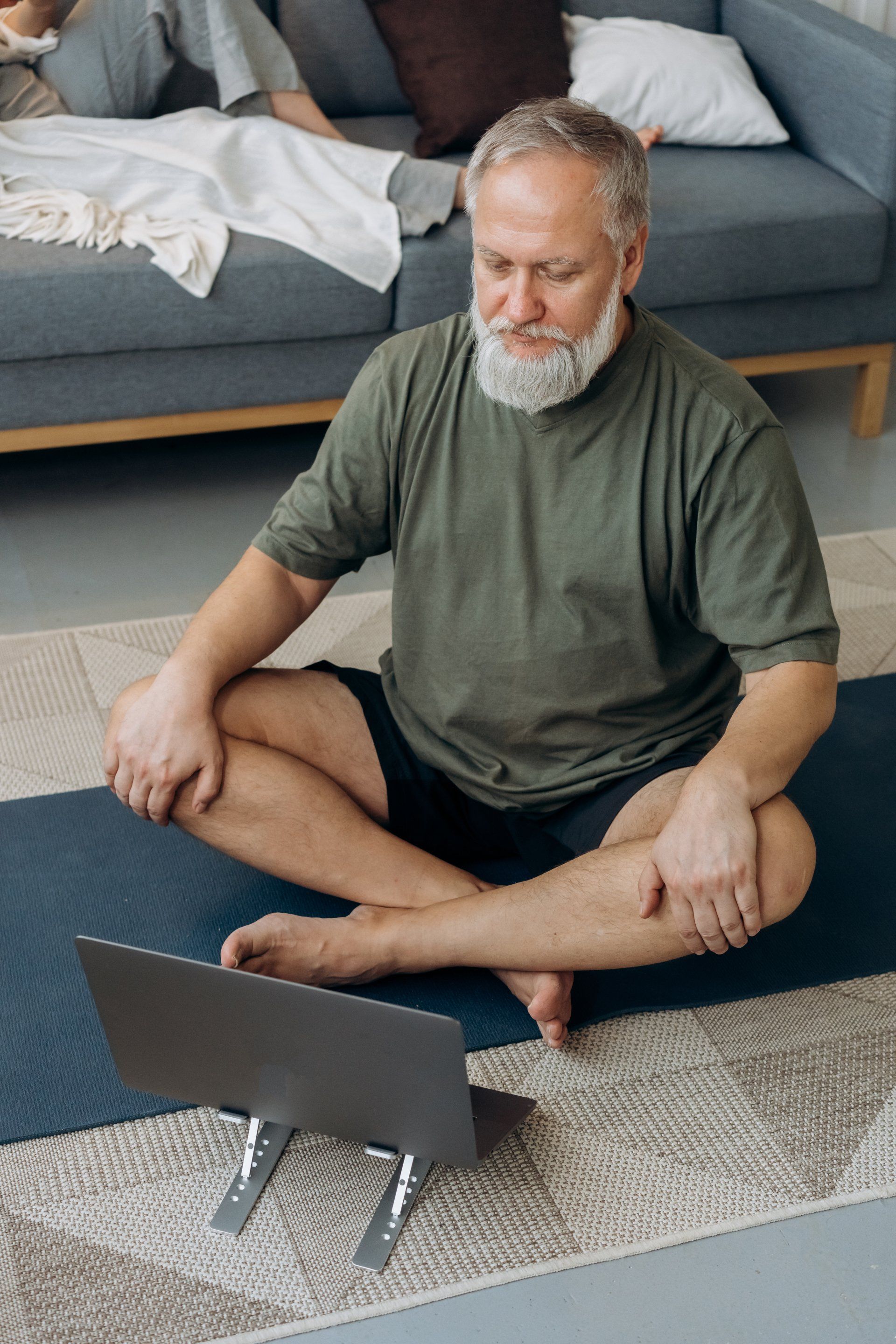 Un hombre está sentado en una colchoneta de yoga utilizando una computadora portátil.