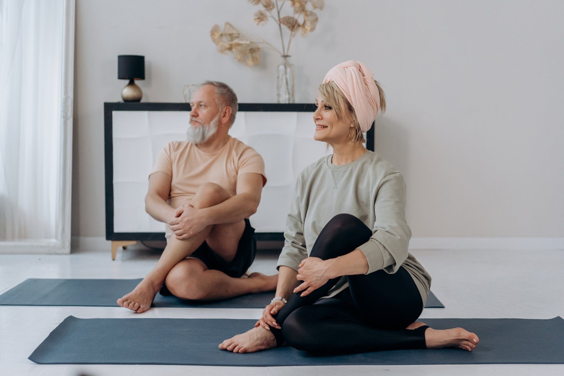 A man and a woman are sitting on yoga mats in a living room.