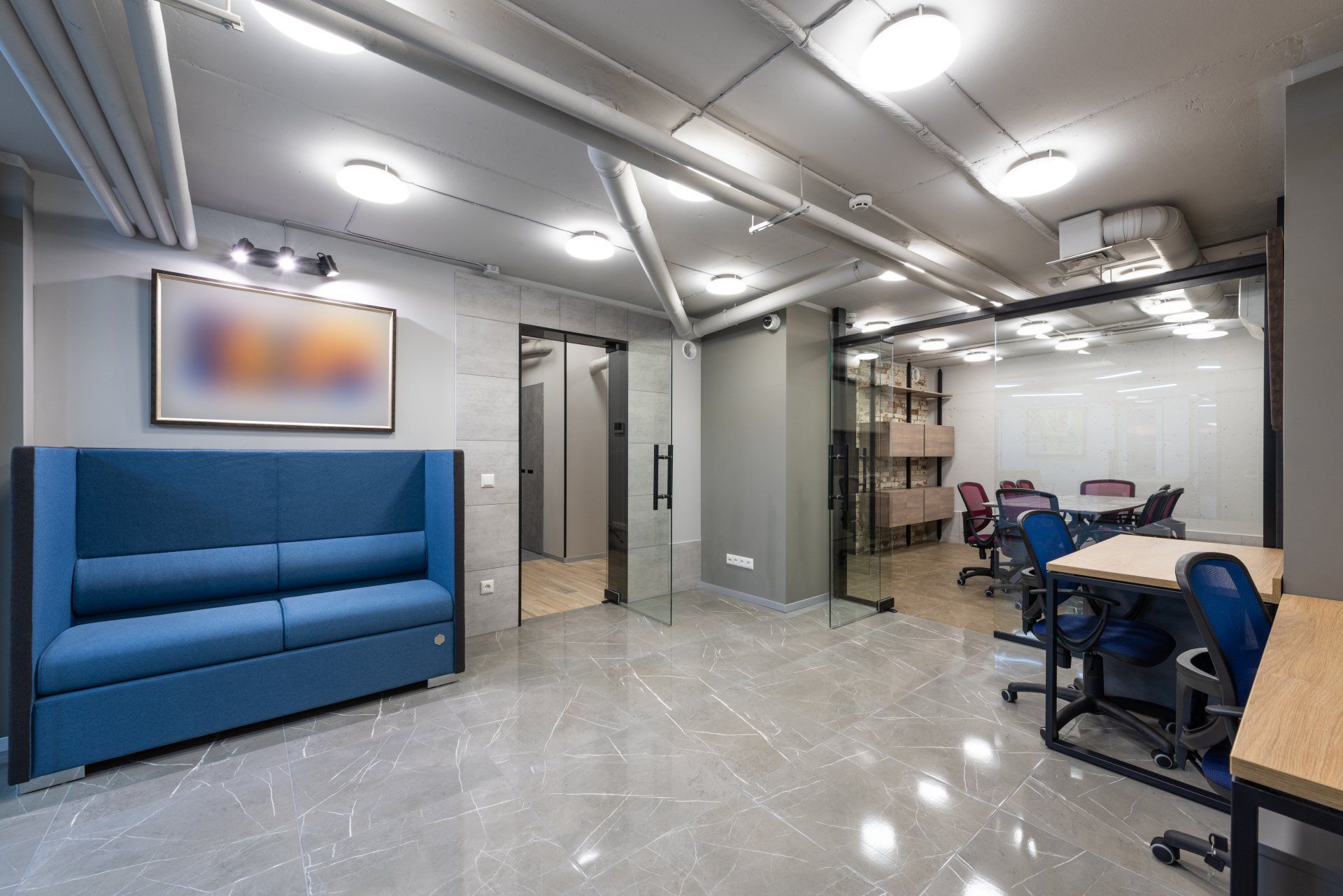 Modern office interior with blue sofa, glass doors, and meeting area. Grey floors and walls.