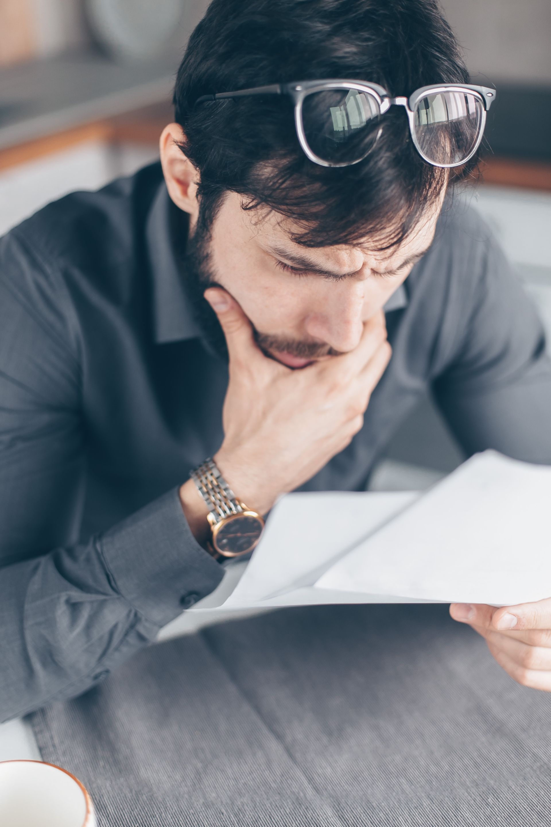 a man wearing glasses is sitting at a table reading a piece of paper .