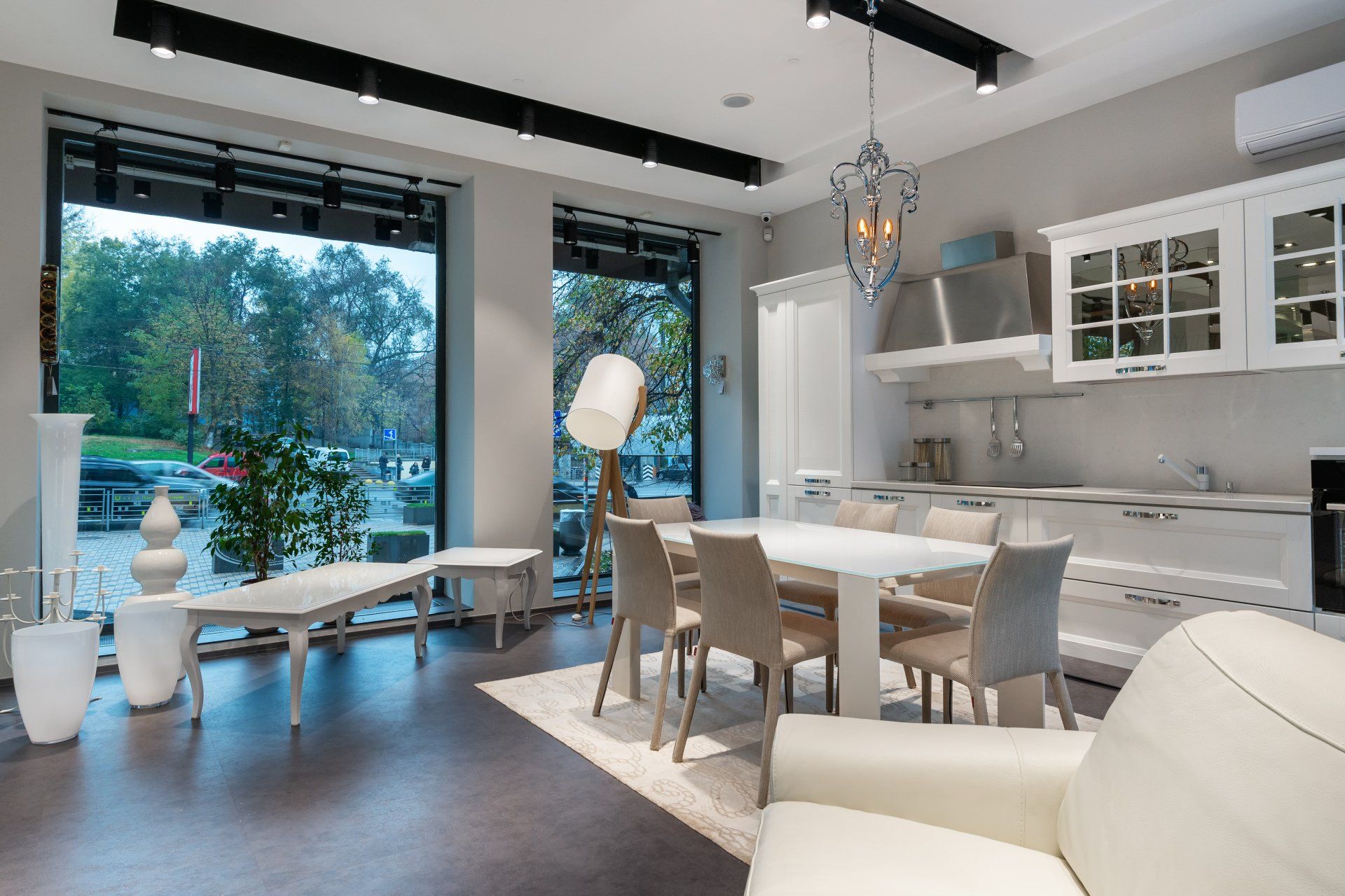 Modern open-plan kitchen and dining room with white cabinets, marble table, and large windows overlooking greenery