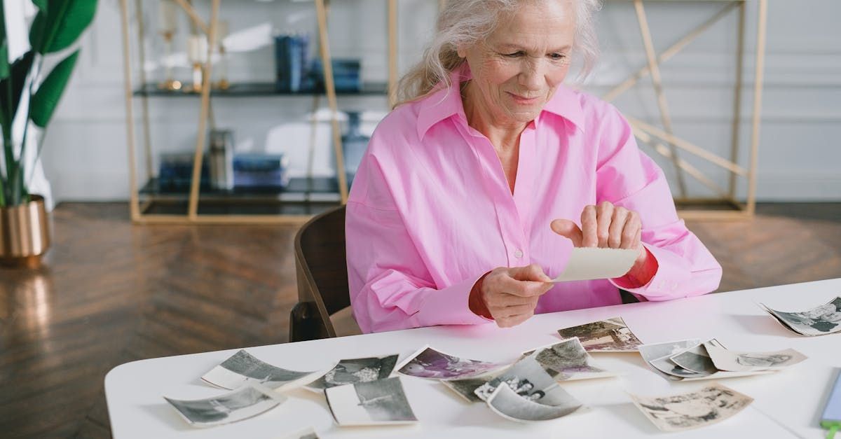 Woman in pink shirt examining black-and-white photo prints on a table in a bright room