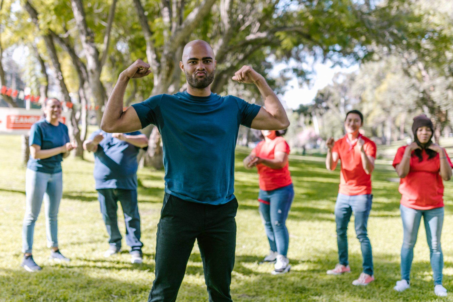 A man is flexing his muscles in front of a group of people in a park.
