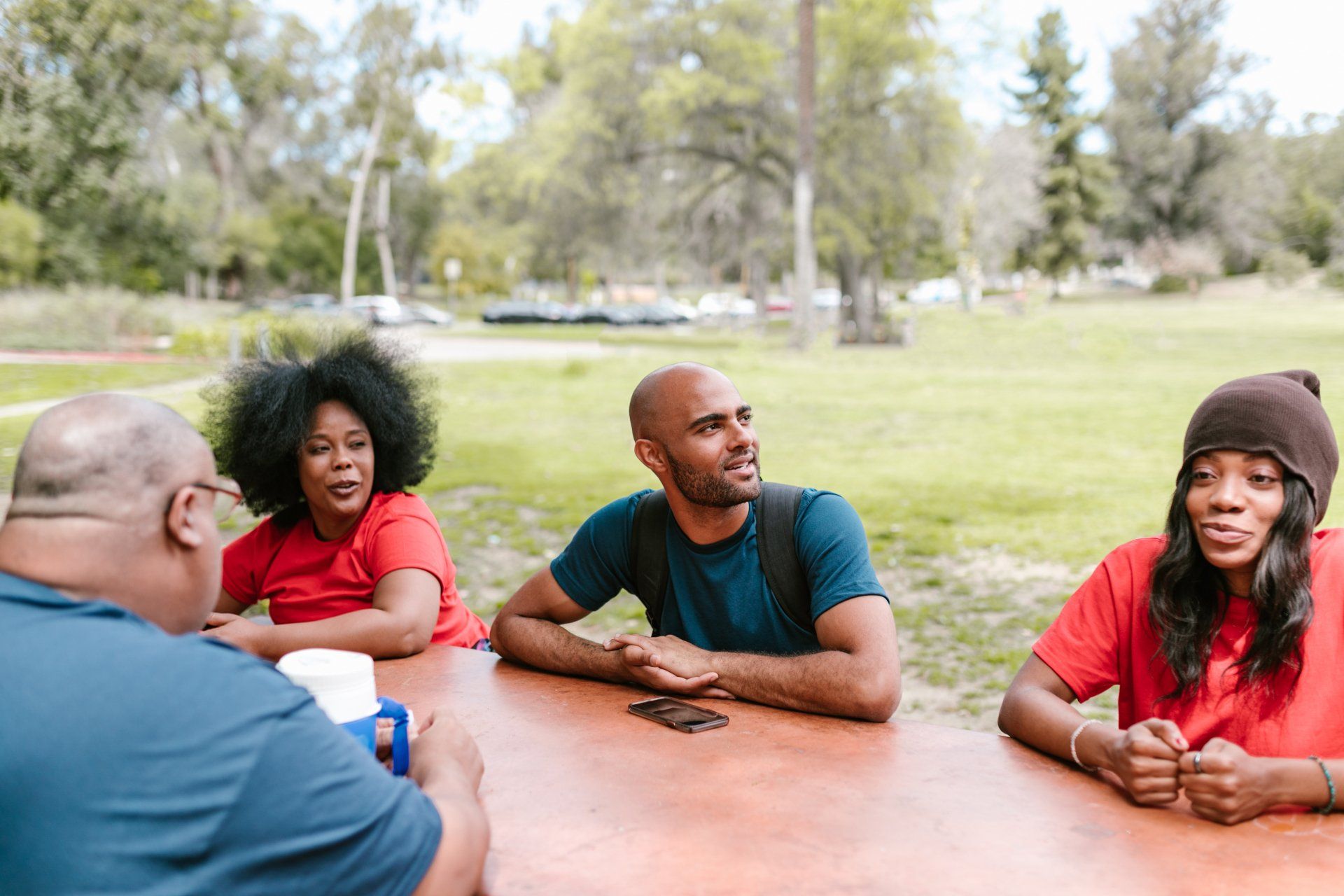 Four people sitting at a picnic table in a park, smiling and talking.