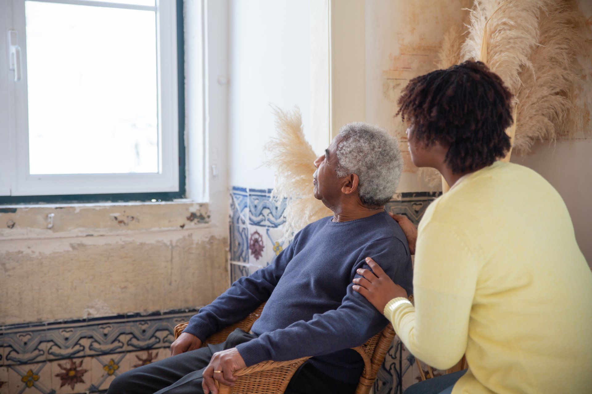 A woman and elderly man looking out a window