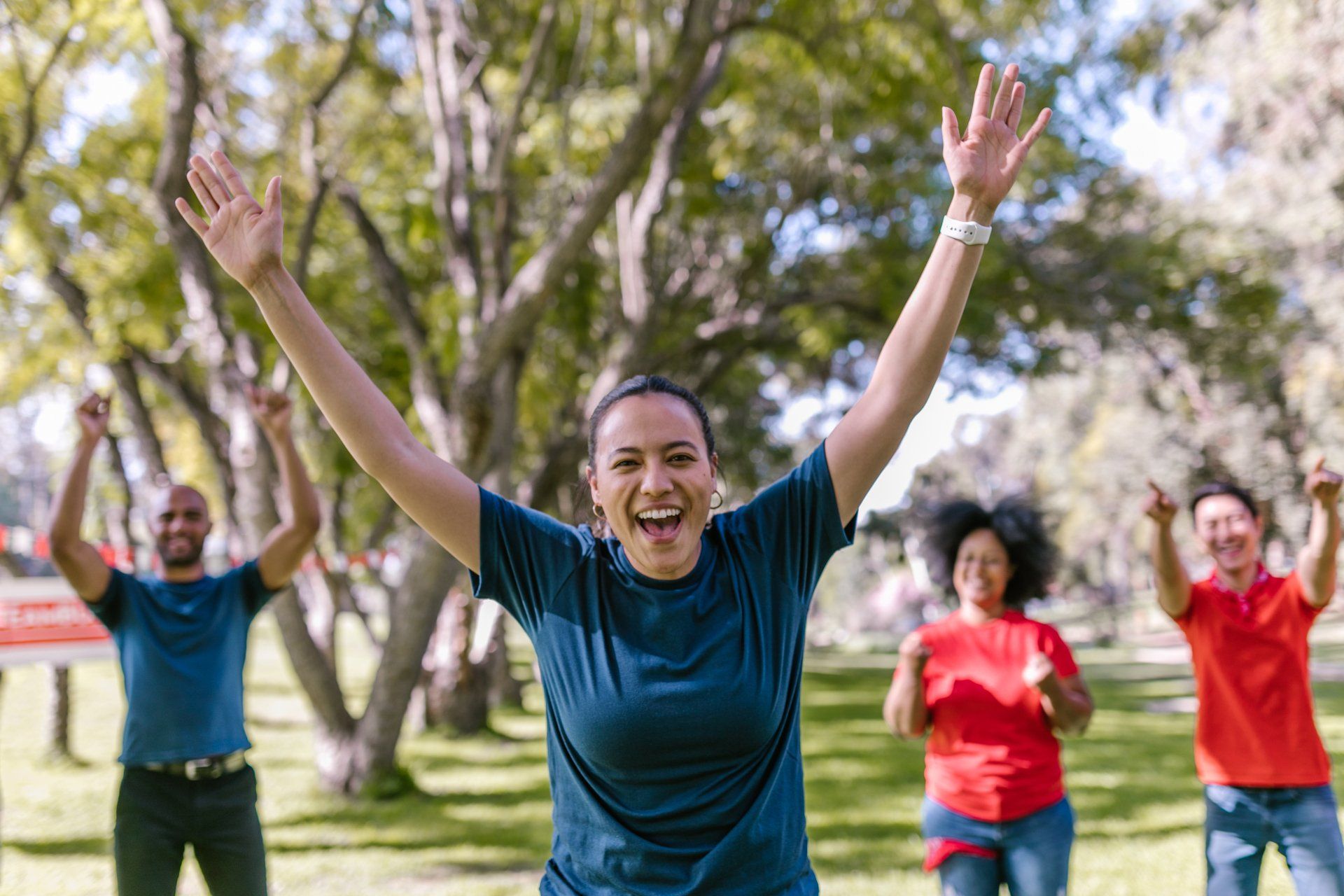 Group of people exercising outdoors, raising arms with excited expressions.