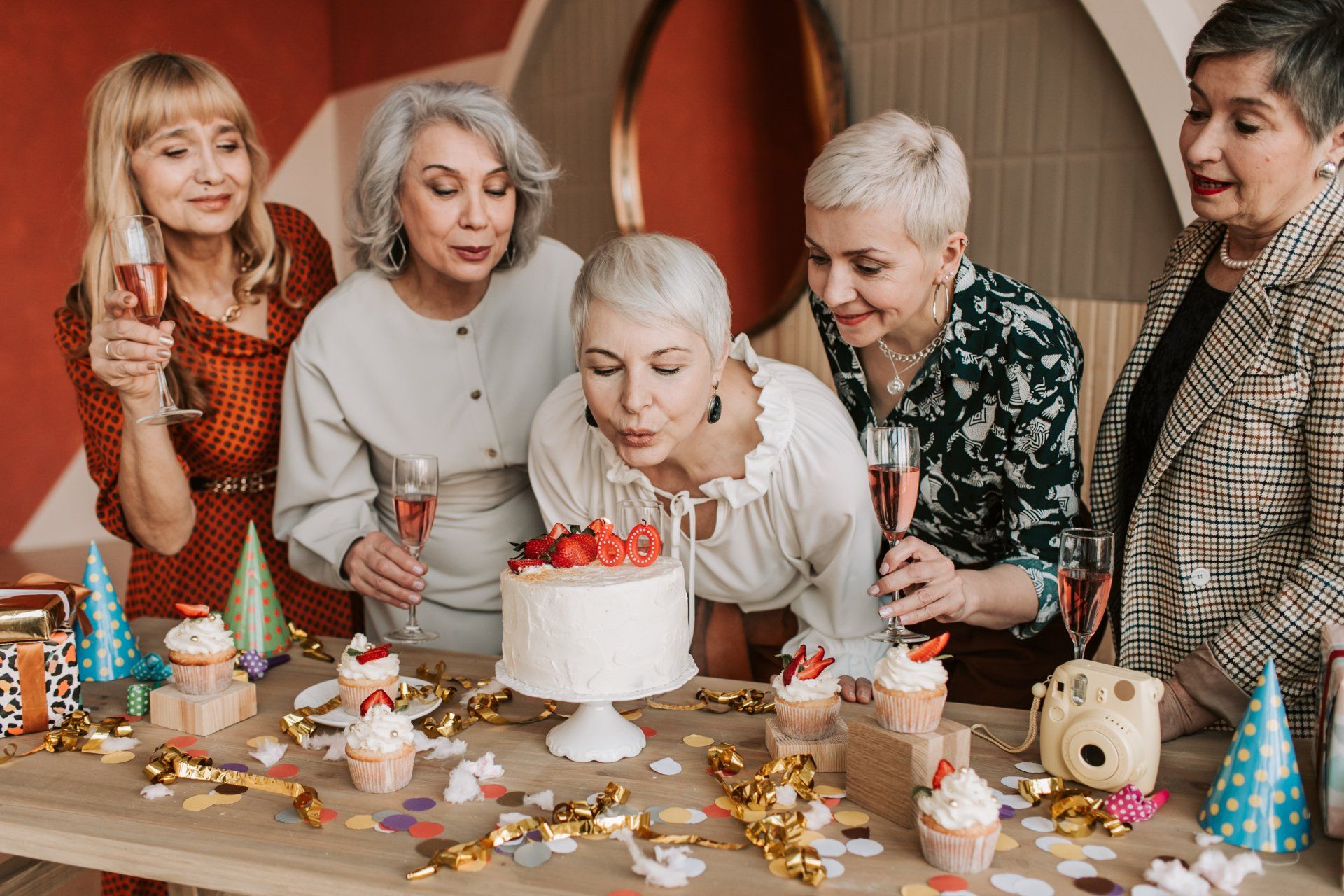 a group of older women are celebrating a birthday with a cake and cupcakes .