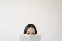 Person peeks over an open book against a plain white background.