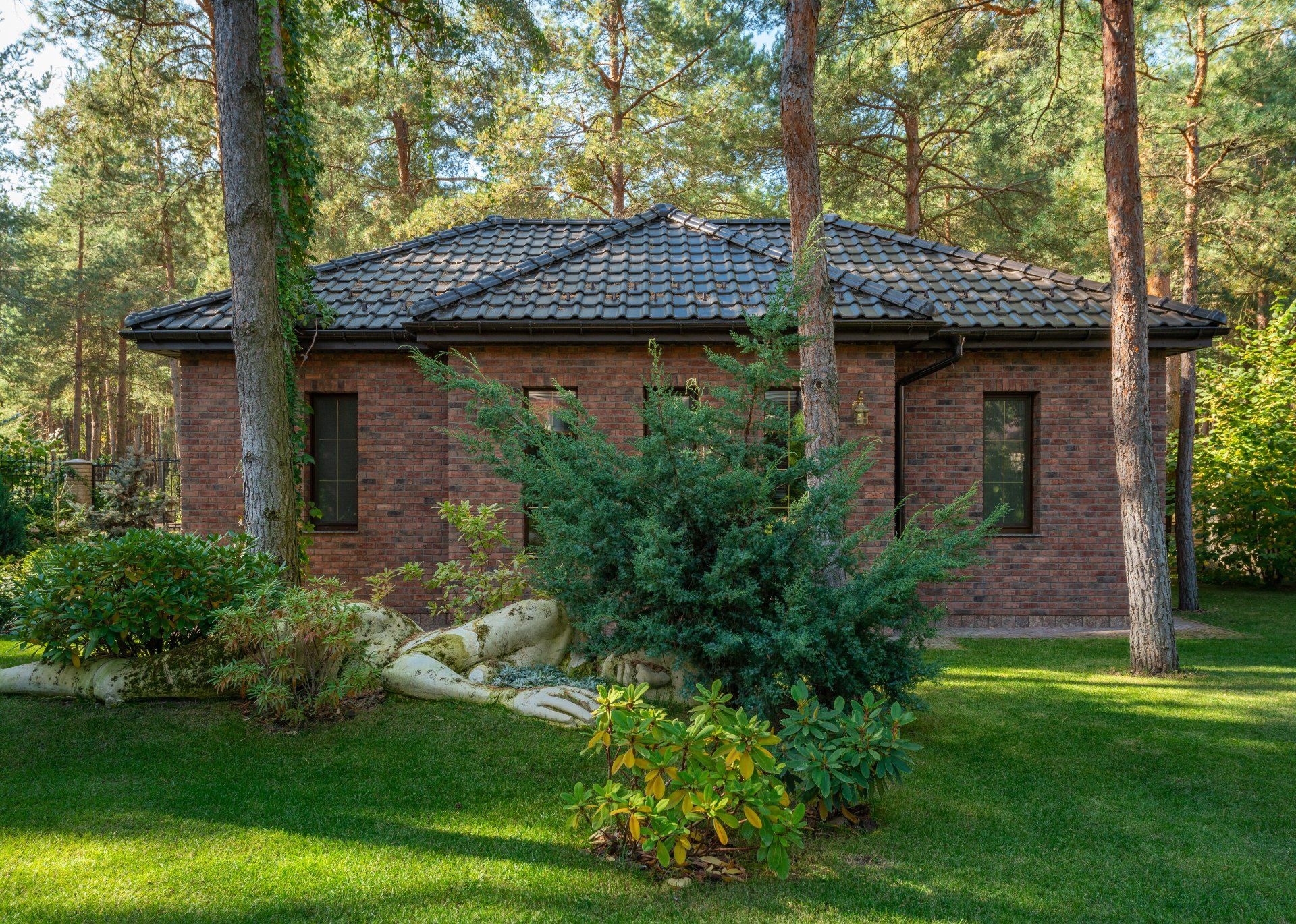 Brick house with dark roof surrounded by trees and green lawn.