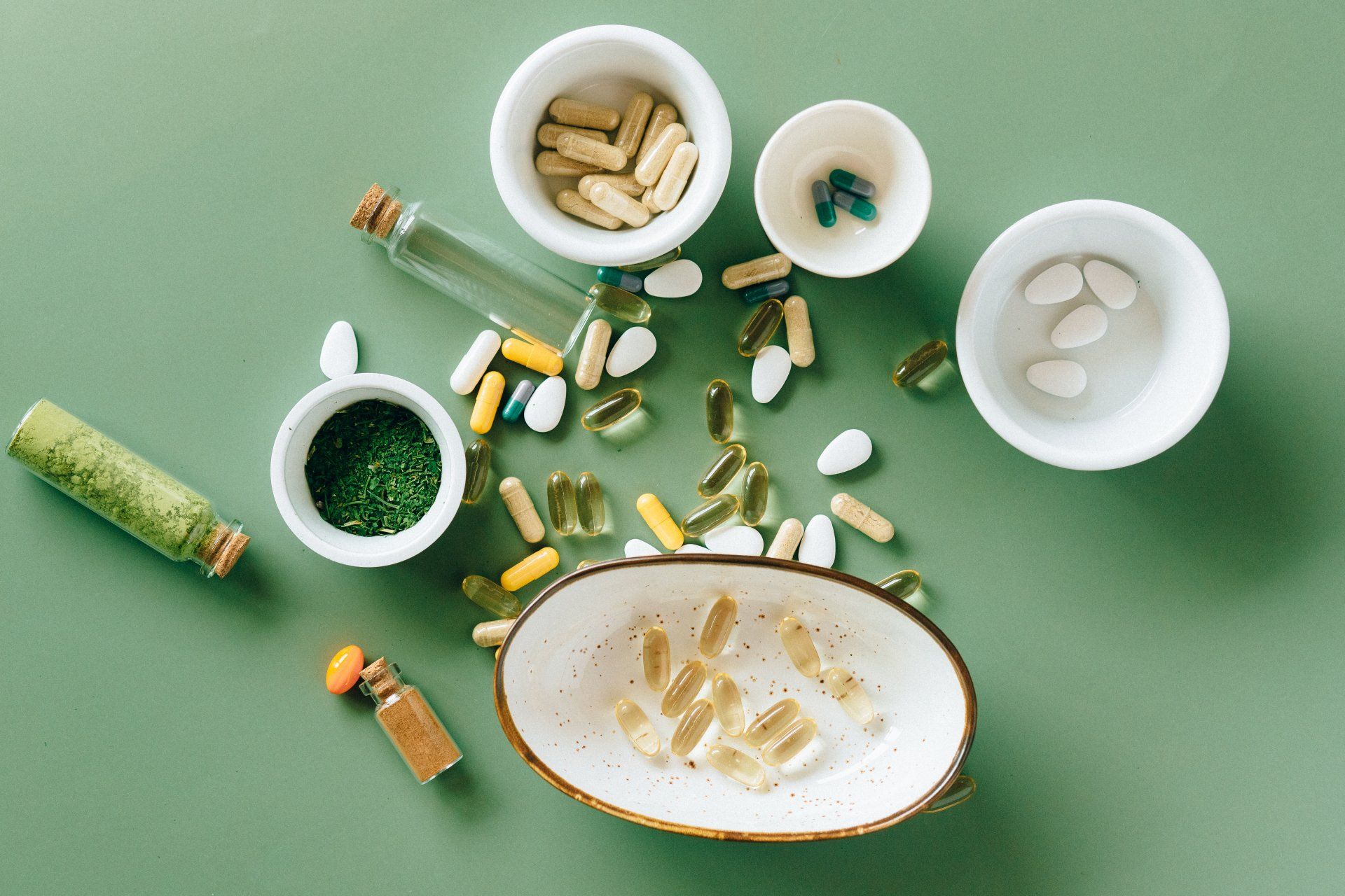 Scattered pills and capsules around white bowls on a green surface, suggesting medication or overdose.