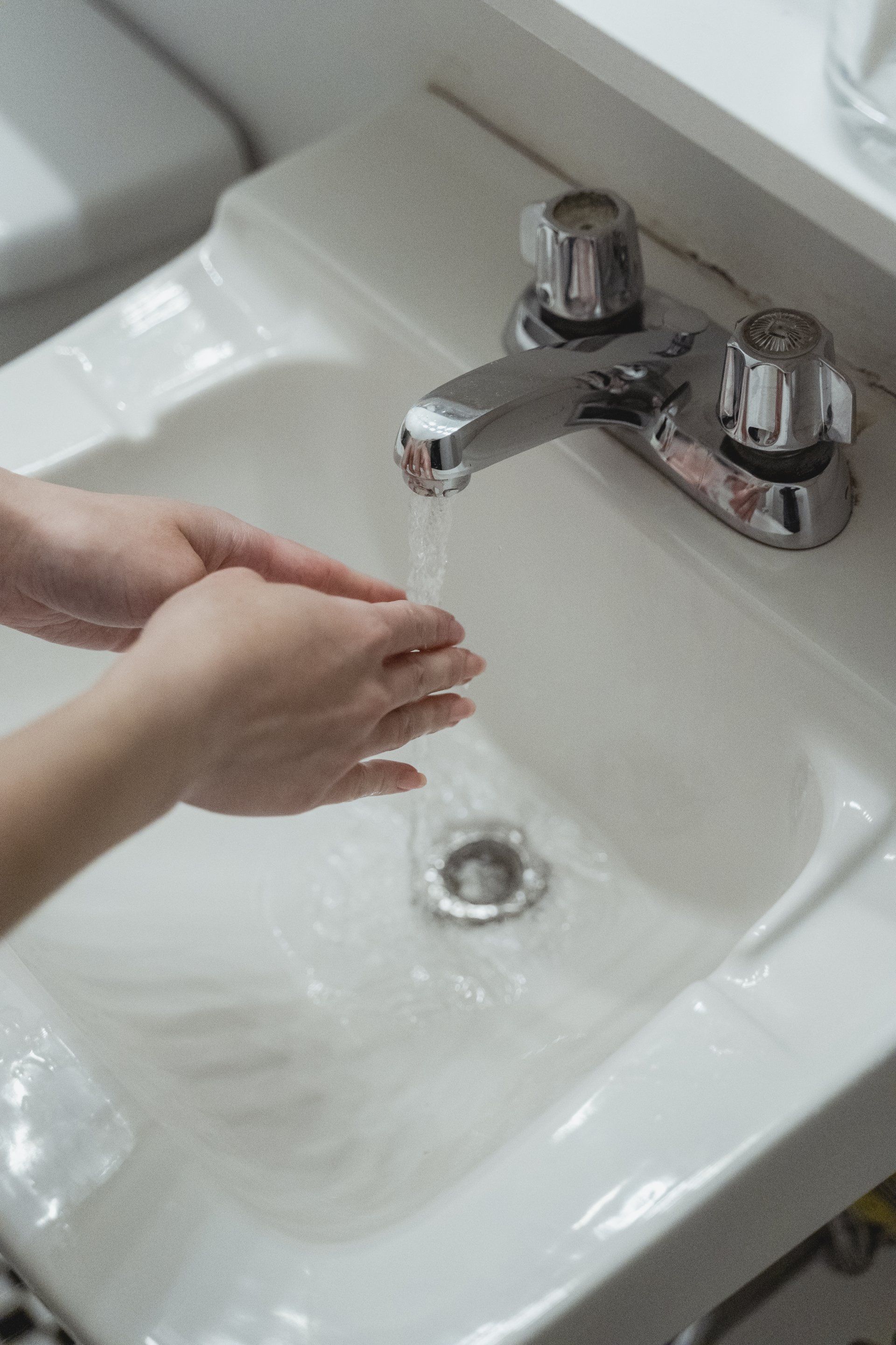 Hands washing under running water in a white sink. Chrome faucet.