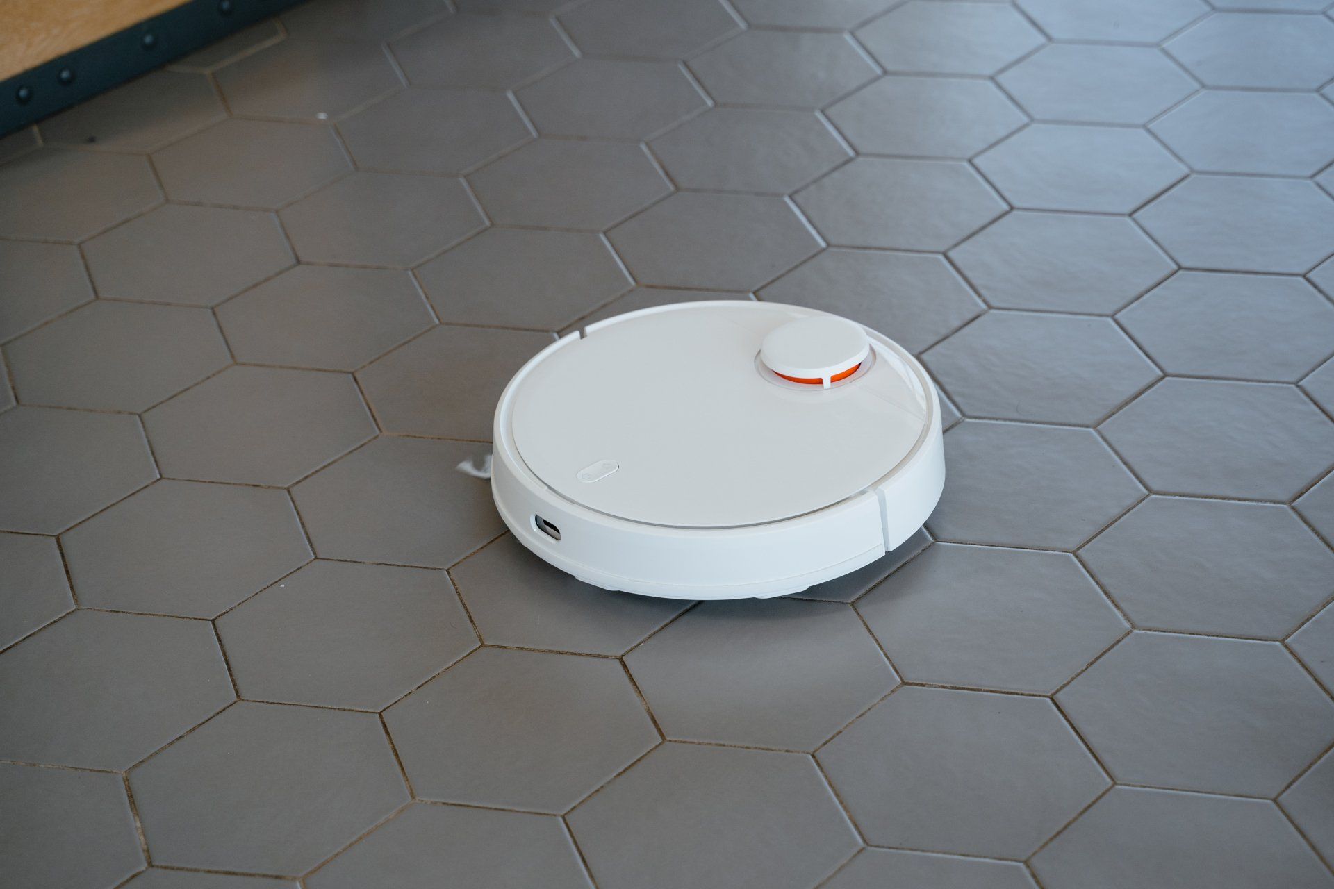 A white robotic vacuum cleaner is sitting on a tiled floor.