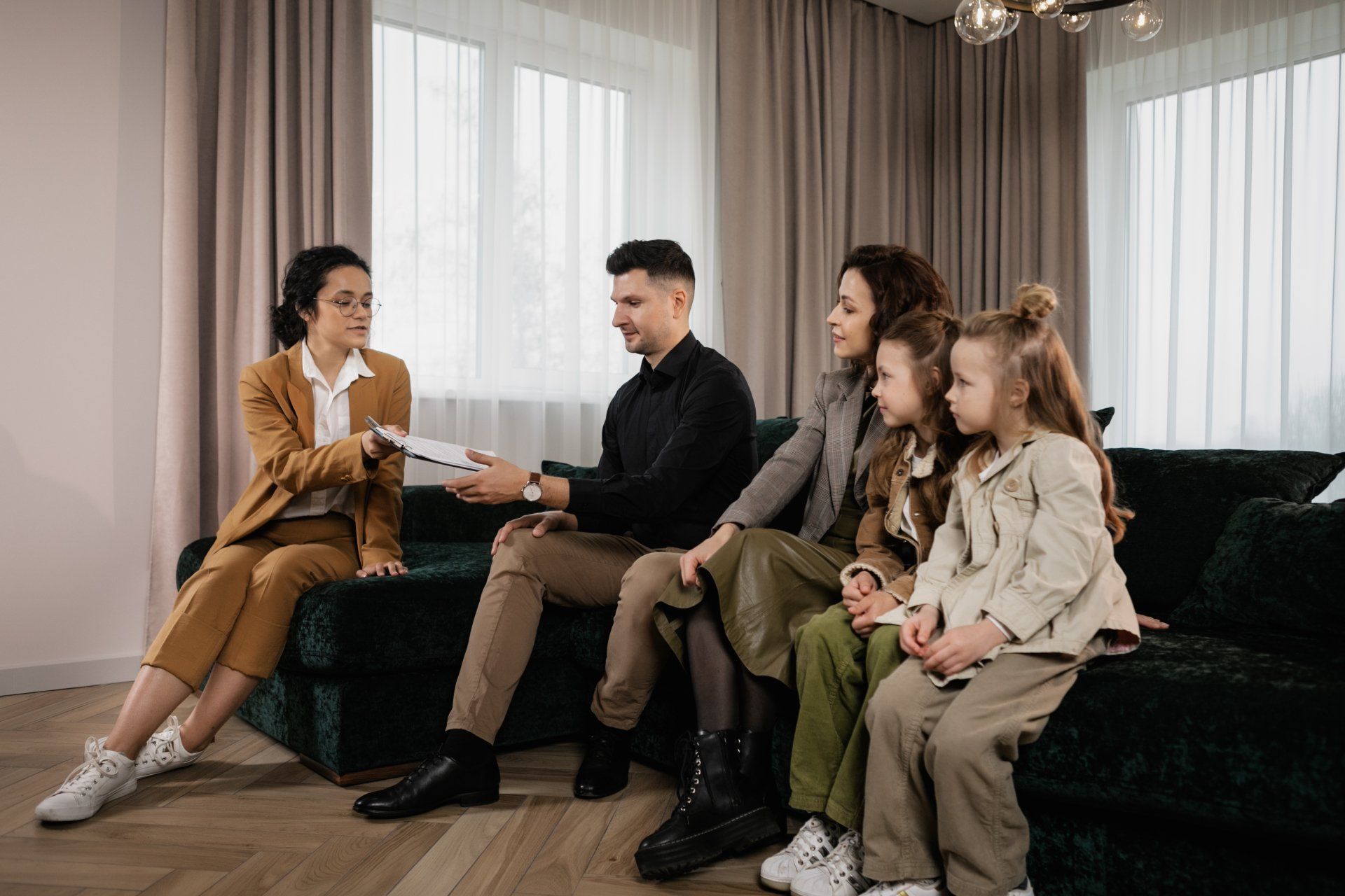 Woman in suit presents documents to a family seated on a green couch in a home. 
