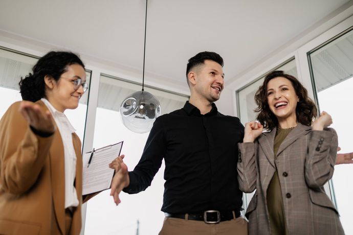 Real estate agent with excited couple in a bright room; they're celebrating a successful deal.