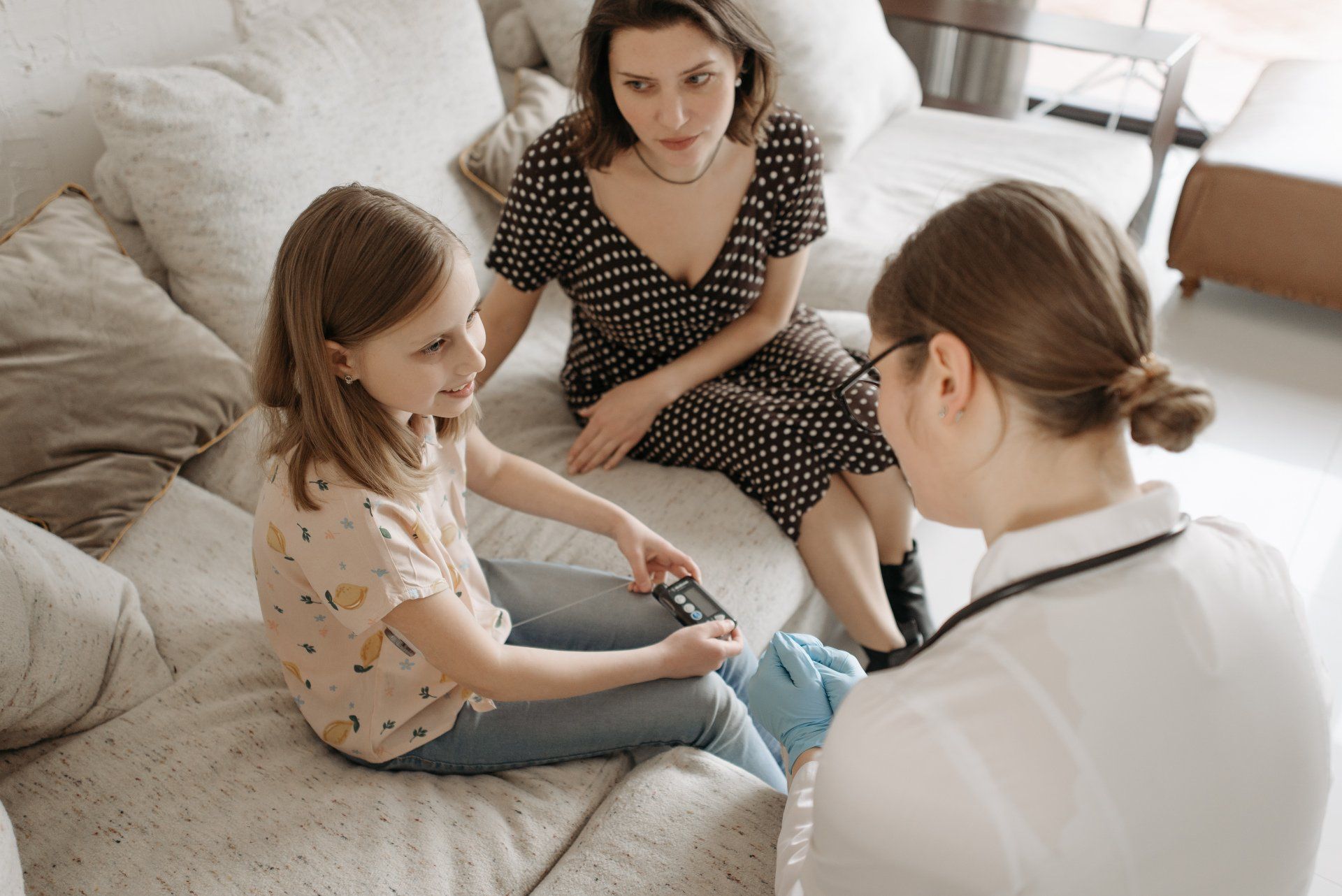 A woman and a little girl are sitting on a couch talking to a doctor.