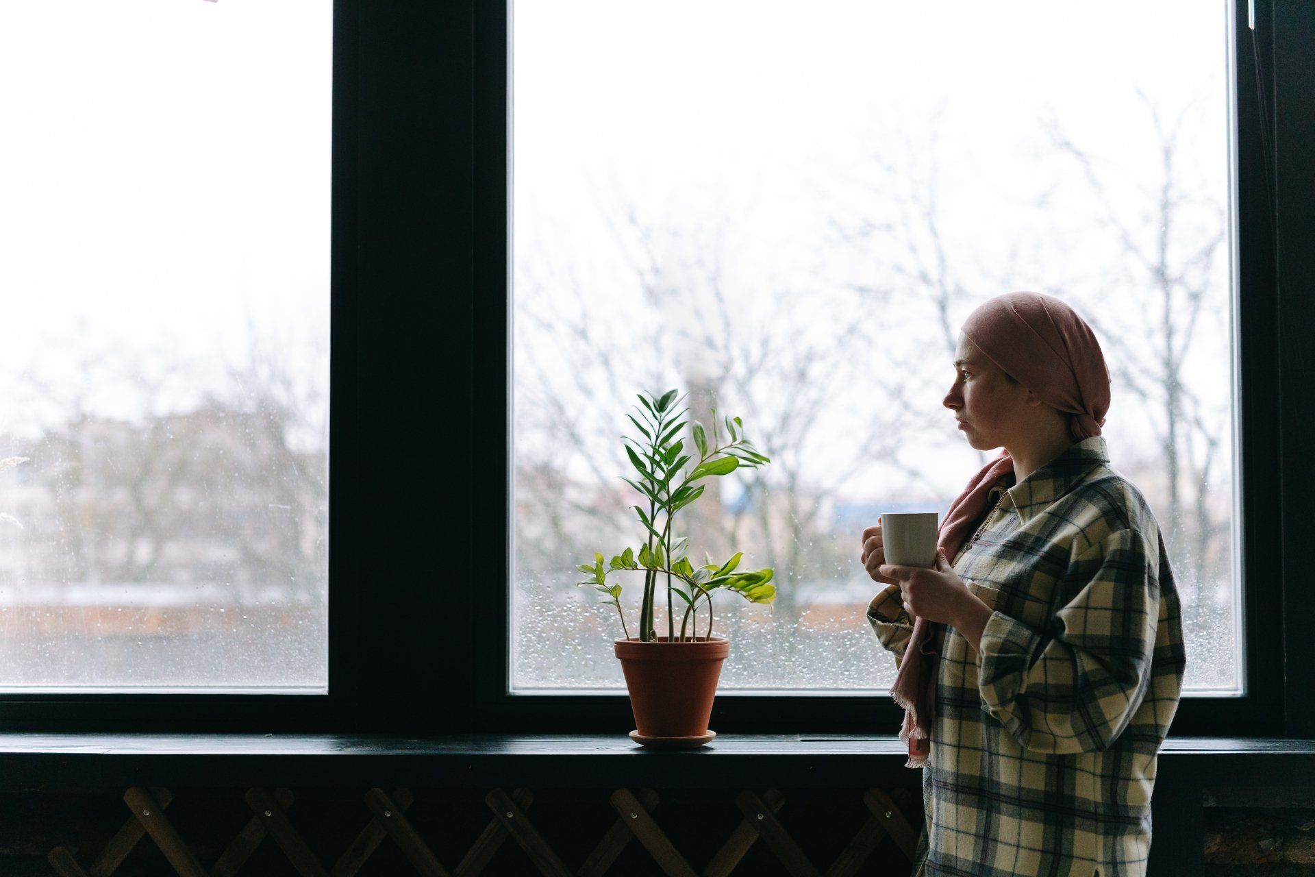 A woman is standing in front of a window holding a cup of coffee.